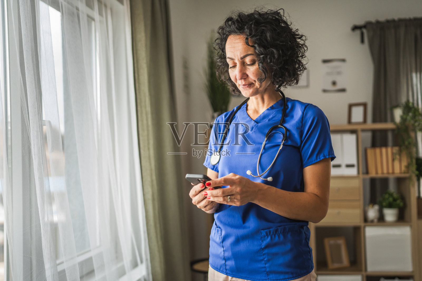 成熟的女性医生在家中站着使用手机照片摄影图片