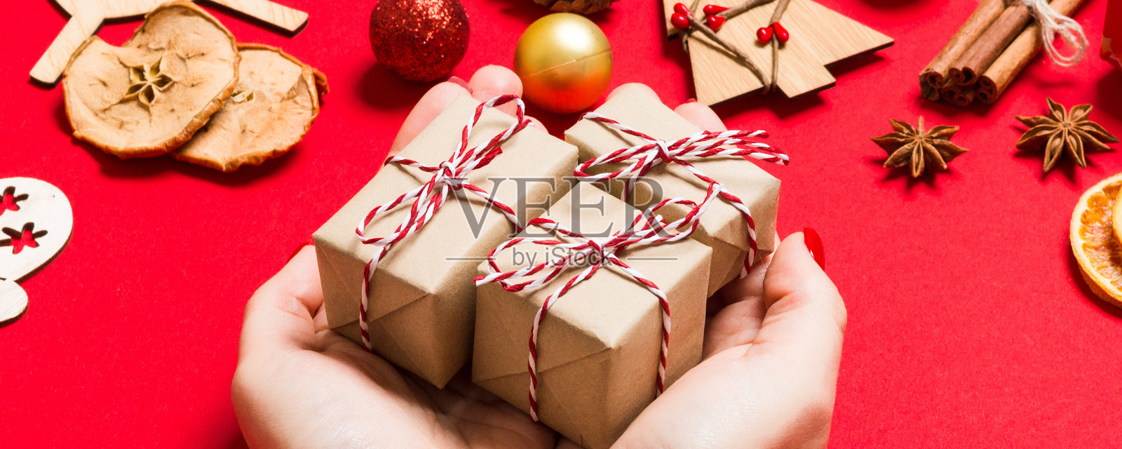从上方看女性手握着圣诞礼物，背景为节日红色。节日装饰。新年假期概念。照片摄影图片