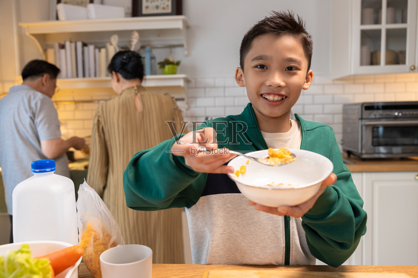儿子在厨房吃早餐，父母正在做饭。照片摄影图片