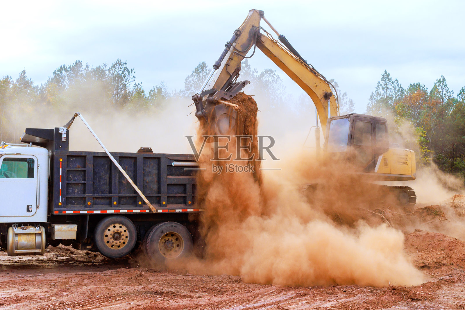挖掘机在建筑工地上将土壤装入自卸卡车。照片摄影图片
