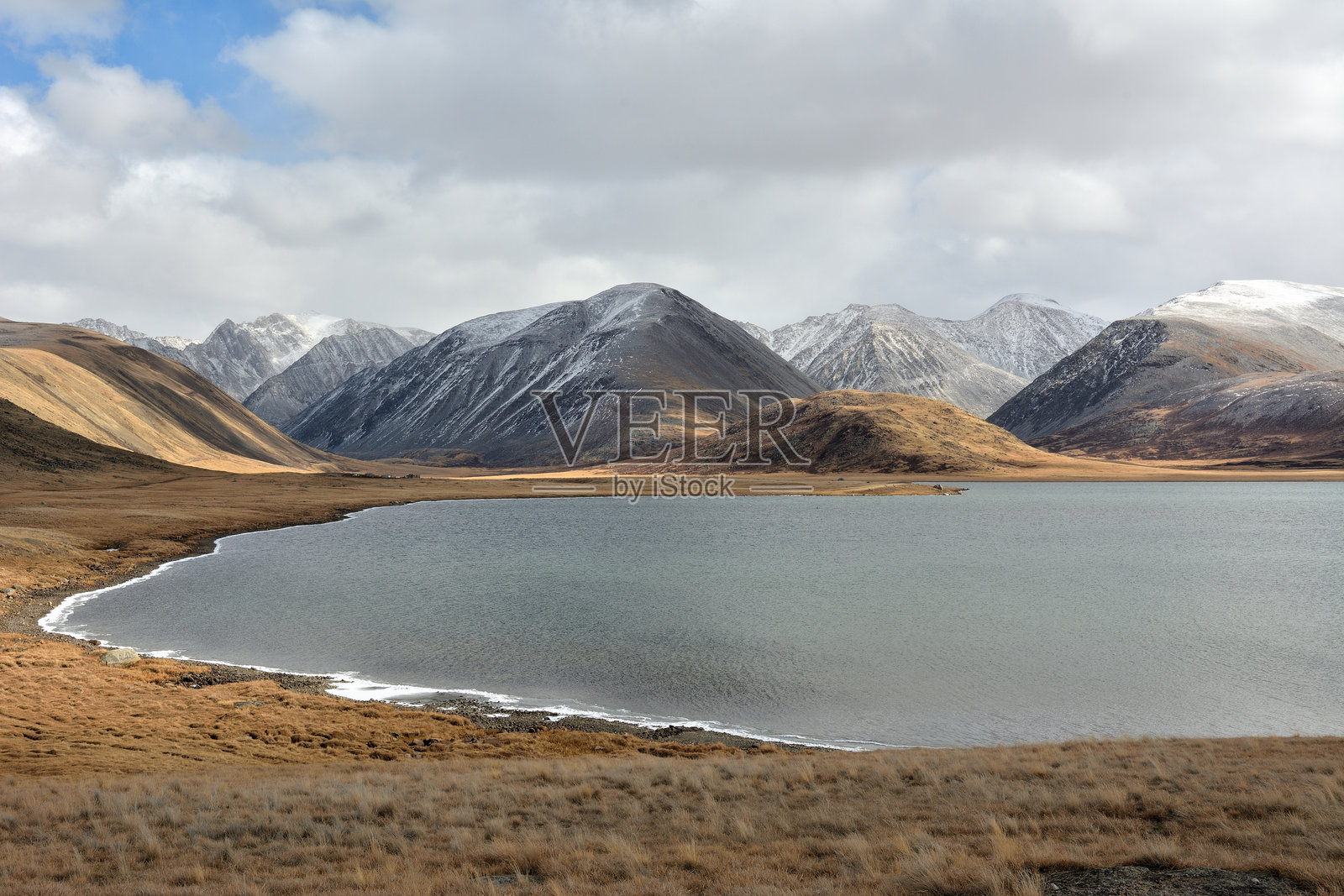 在秋天的日子里，冰封的大湖岸边位于无尽的草原上，四周被高山环绕。照片摄影图片