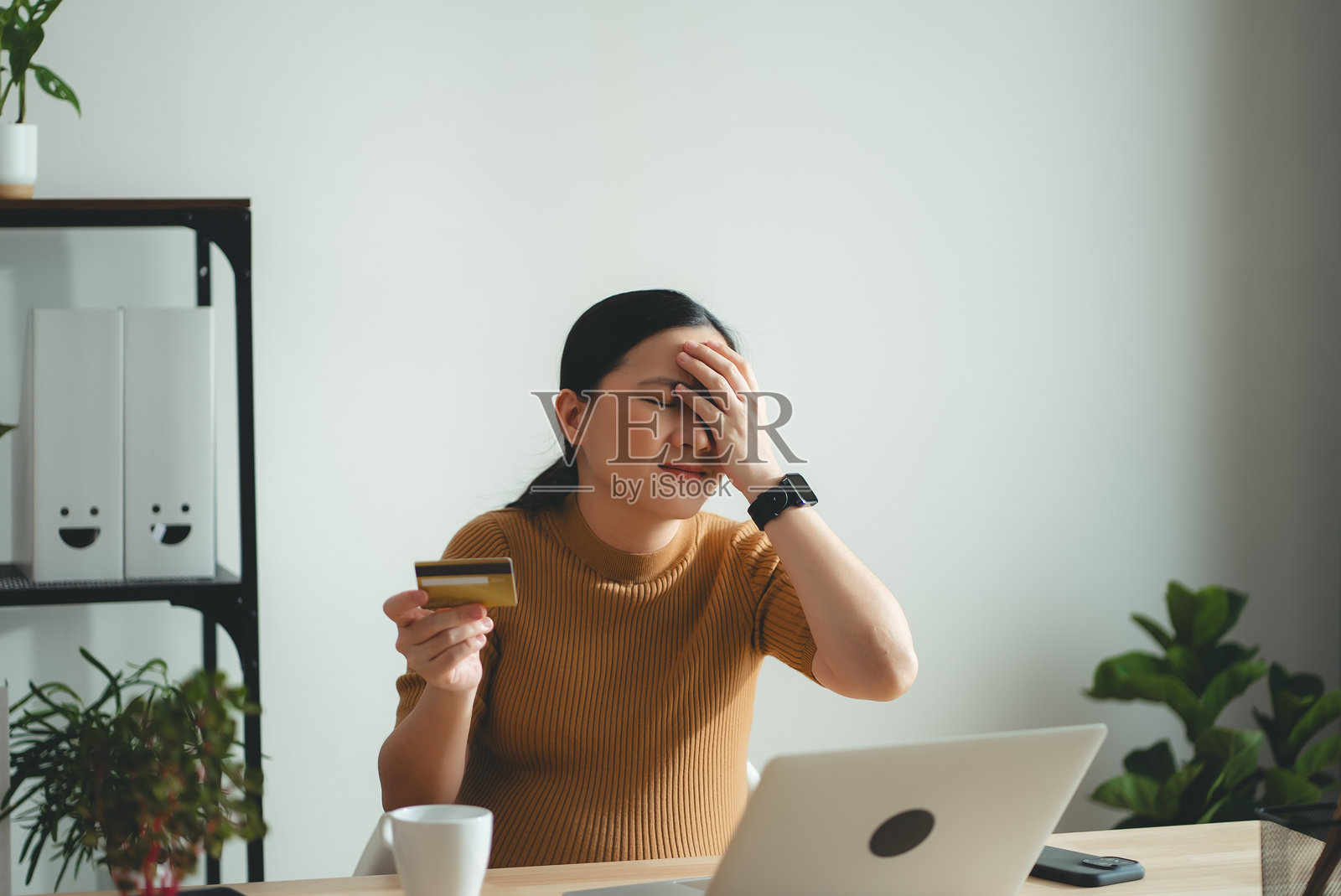 亚洲孕妇手持信用卡，使用笔记本电脑时遇到在线购物和支付问题。照片摄影图片