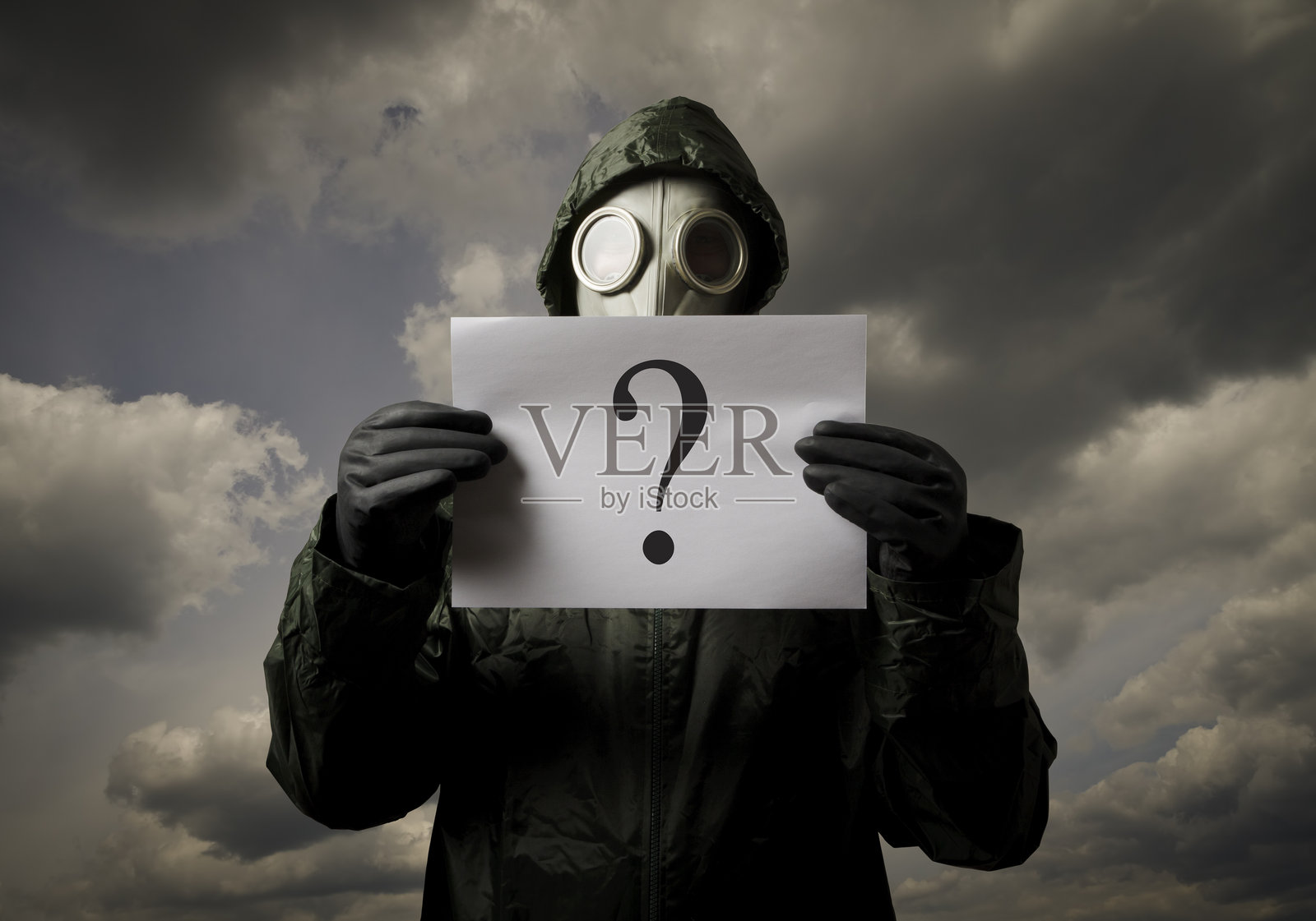 戴着防毒面具的人手持纸张，站在阴 cloudy 的天空下。照片摄影图片