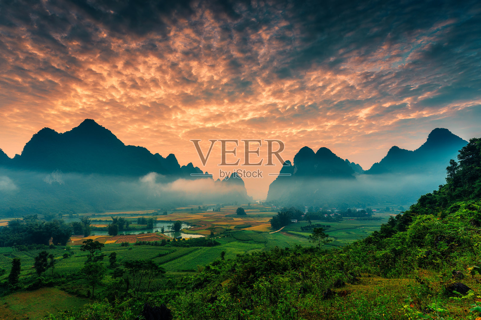 丰南谷中，山脉上空绚丽的日出景观，雾气弥漫，河流蜿蜒，传统村庄静谧。照片摄影图片