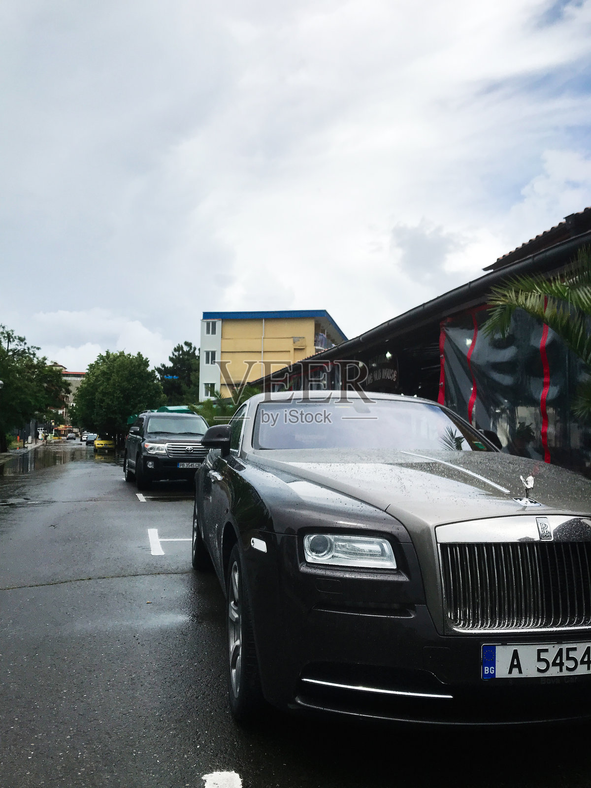 豪华的劳斯莱斯幻影轿车停在雨中的城市街道上,天空阴云密布。照片摄影图片