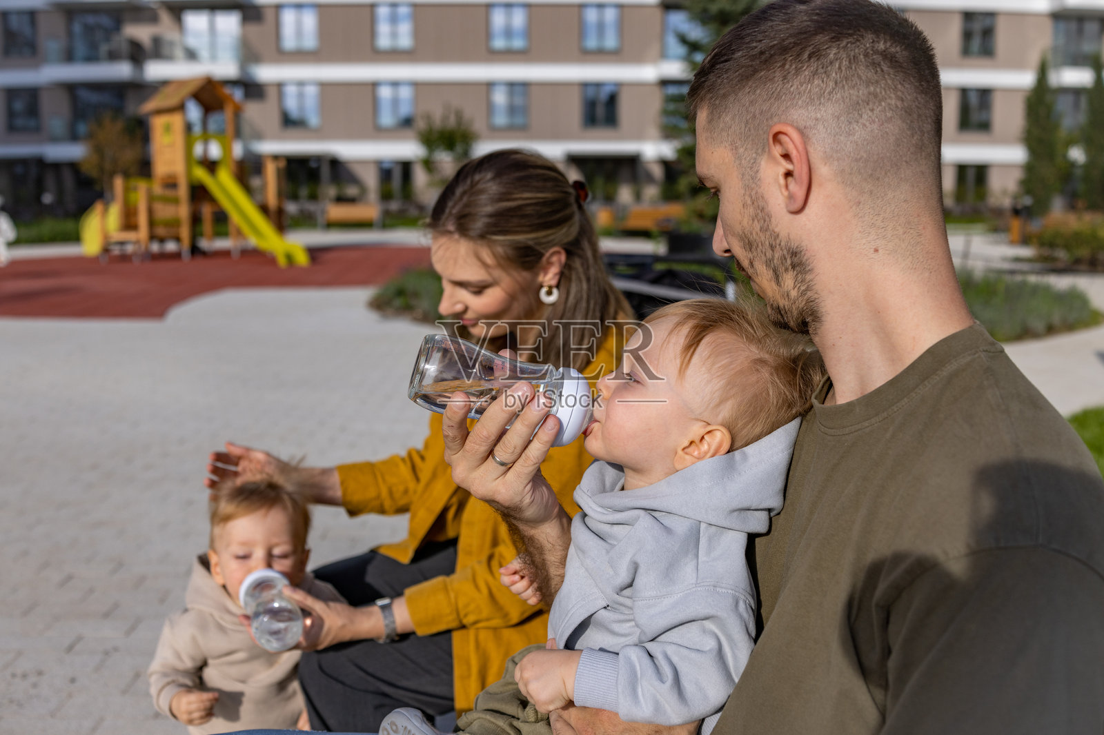 幼儿们舒适地坐在长椅上，和父母一起喝水。照片摄影图片