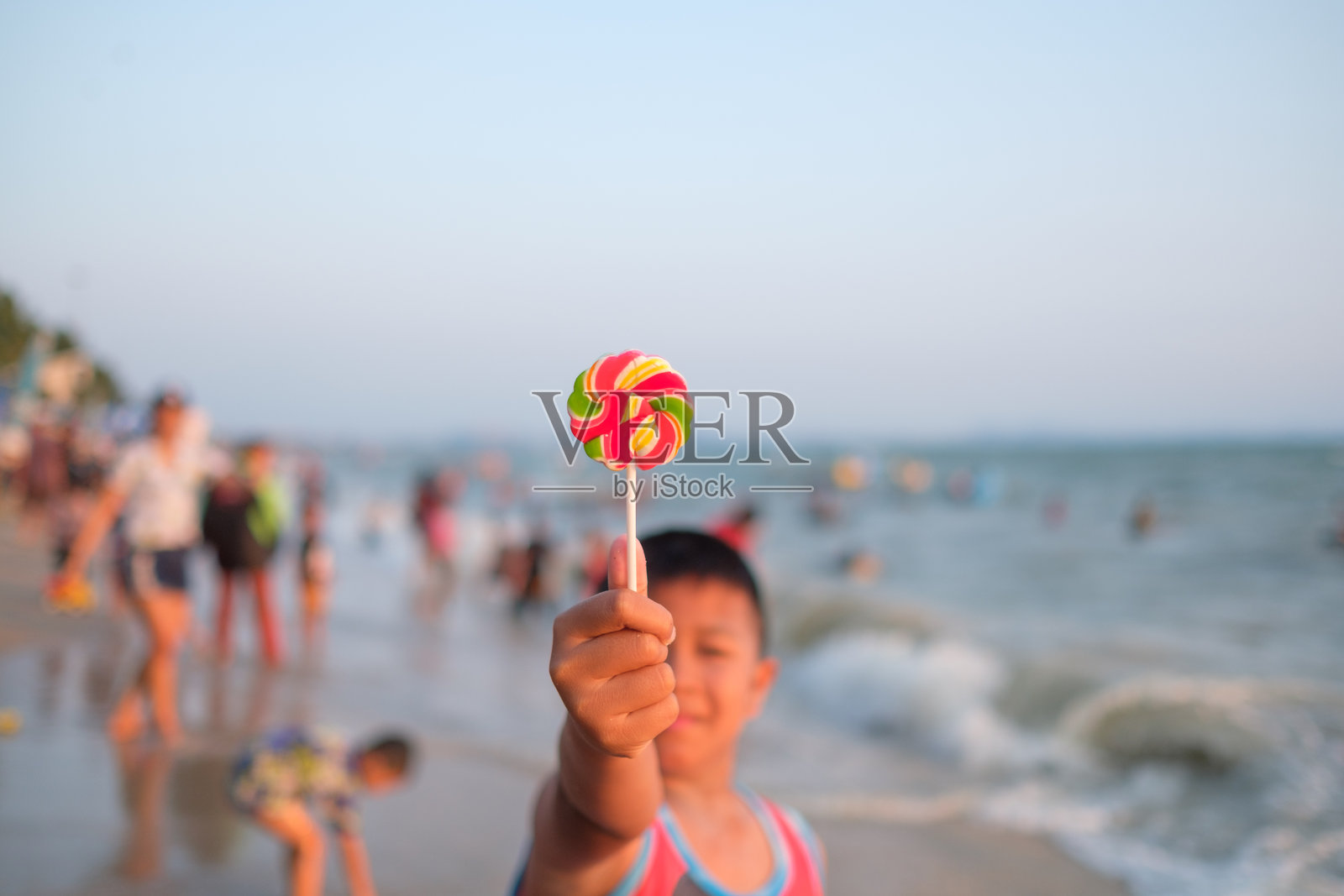 男孩在海滩上举着棒棒糖，背景是天空照片摄影图片