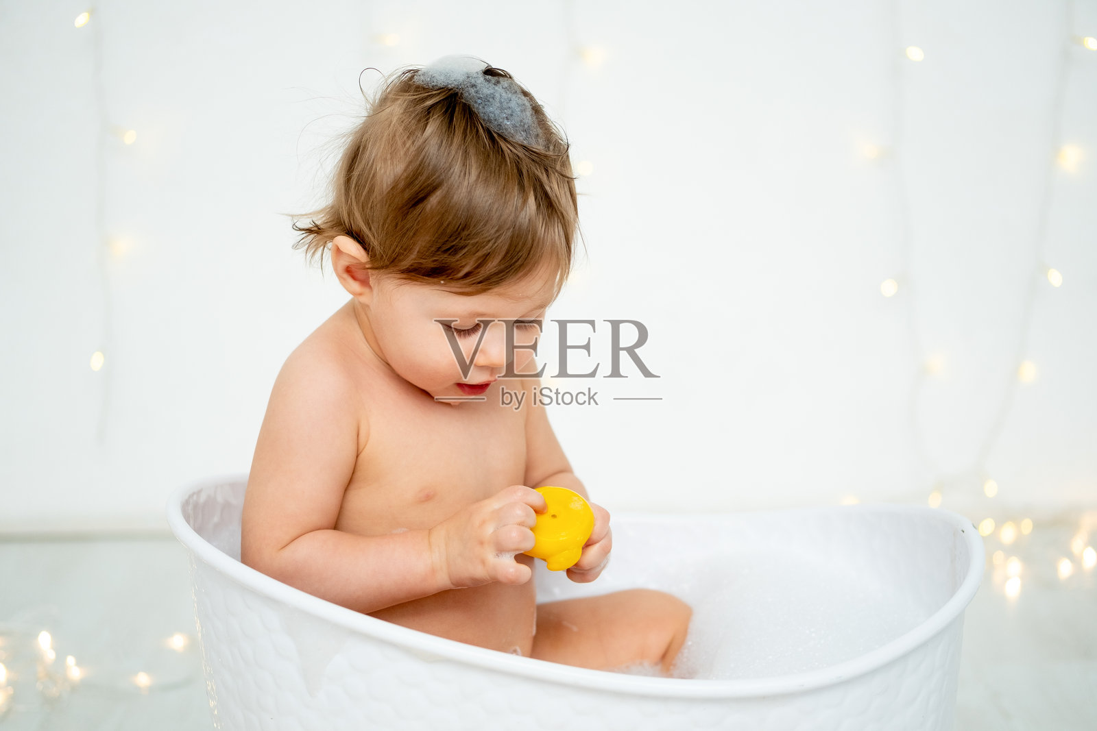一个小男孩在泡泡浴中洗澡，玩着橡皮鸭，背景为白色孤立，留有文字空间。一个快乐的小孩正在清洗文字区域。照片摄影图片