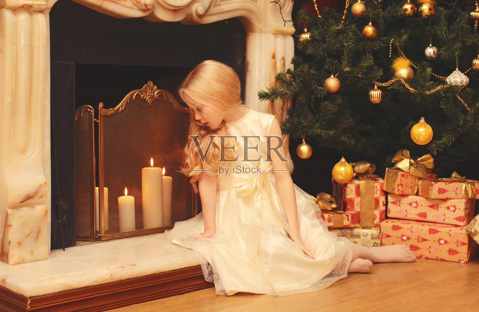 快乐的小女孩坐在家里的圣诞树和壁炉旁，身边有一个节日礼物盒。照片摄影图片