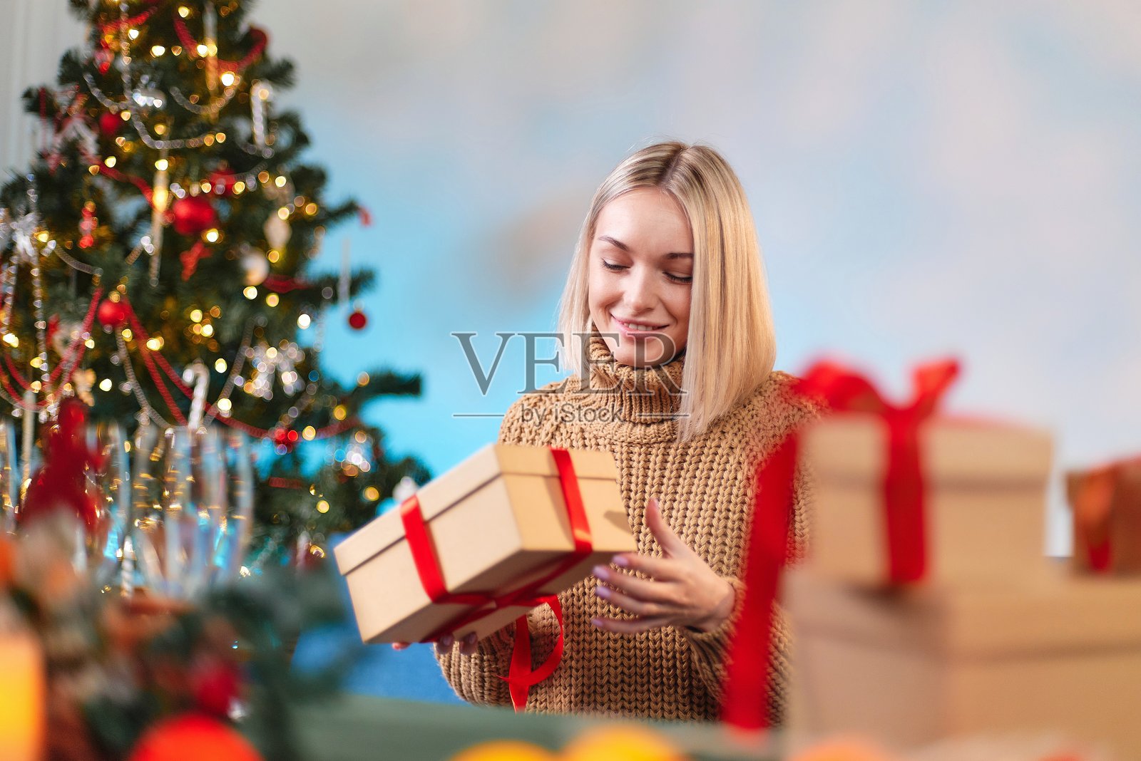 一位年轻女性手中拿着一个系着红色丝带的新年礼物。特写镜头展示一位女性手握着一个红丝带的圣诞礼物盒。节日概念。一位穿着白色毛衣的年轻女孩手中拿着一个新年礼物盒。照片摄影图片