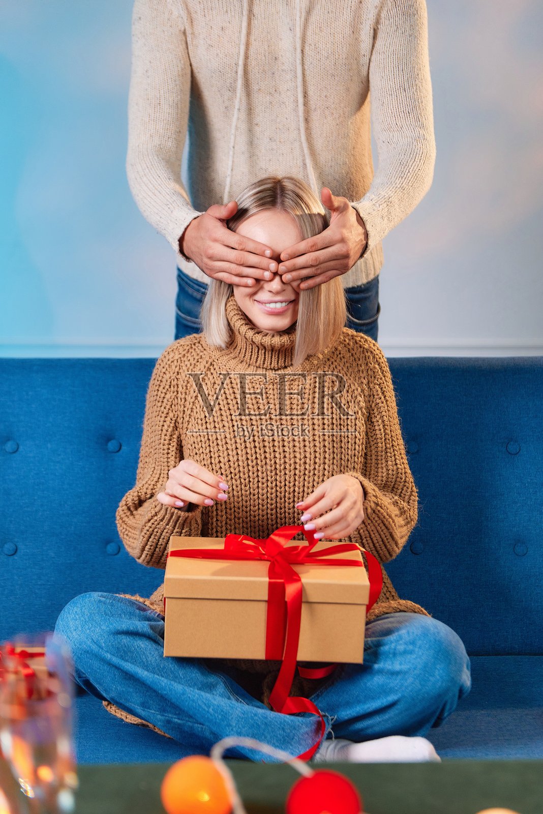 男人用手遮住女人的眼睛，手里拿着圣诞礼物盒。照片摄影图片