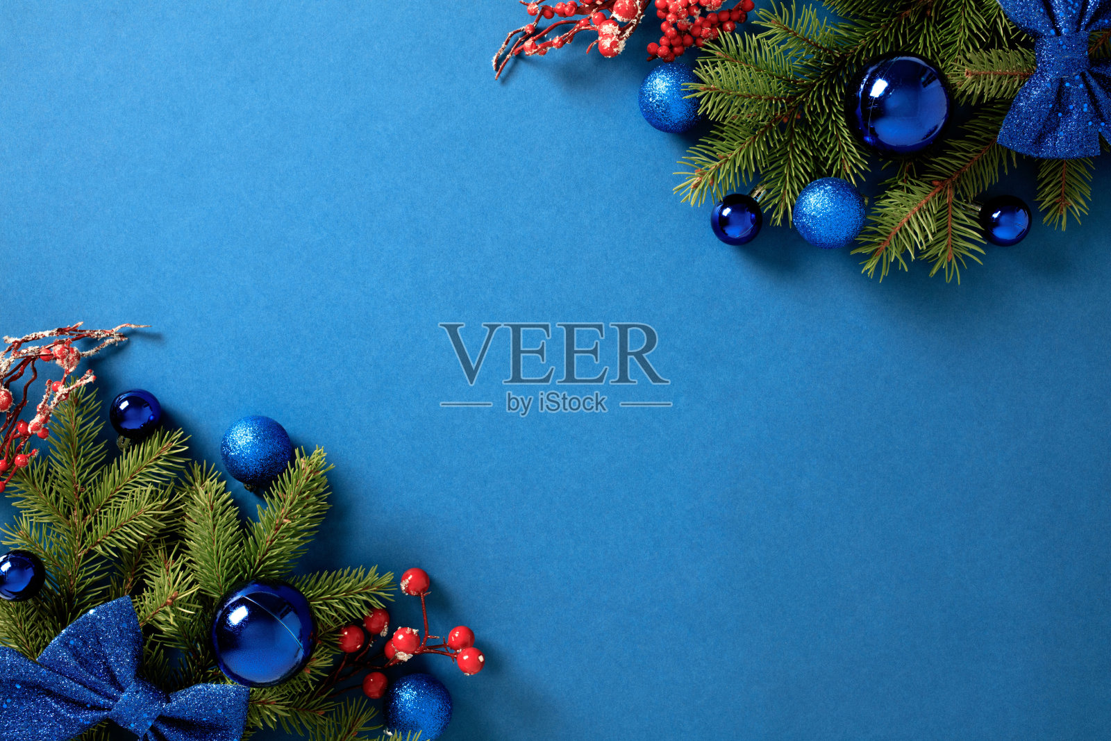 圣诞背景，蓝色装饰品、红色浆果和松枝在鲜艳的蓝色背景上照片摄影图片
