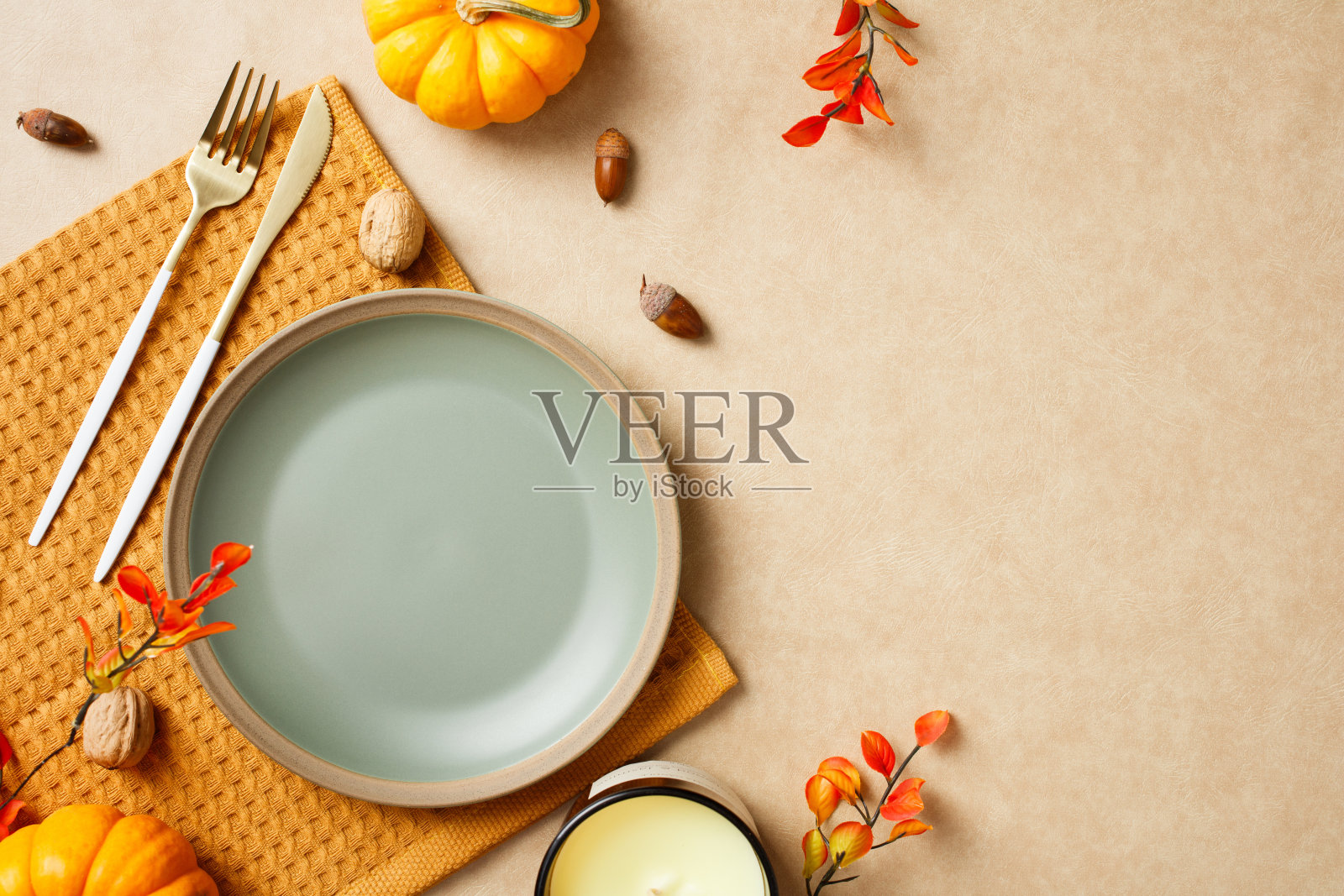 秋季餐桌布置，空盘子、金色餐具、南瓜、橡果、核桃和红橙色的叶子摆放在米色表面上照片摄影图片