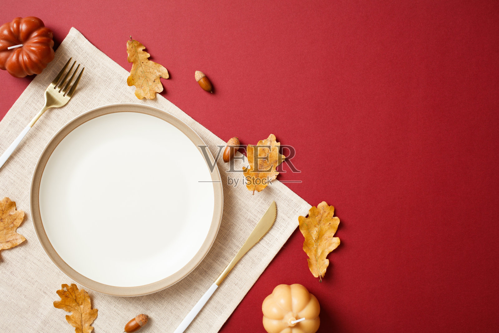 从上方俯视的餐桌布置，白色盘子、金色餐具和秋季装饰，背景为深红色。照片摄影图片