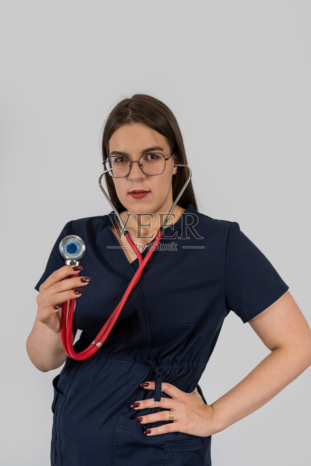 穿着蓝色医疗服的年轻白人护士在工作室摆姿势，背景为单色。照片摄影图片