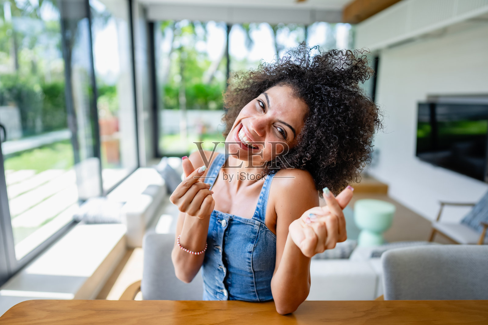 一位非洲裔年轻女性坐在现代客厅里，微笑着使用笔记本电脑进行视频通话。她有着卷曲的头发，看起来在网上很开心。照片摄影图片