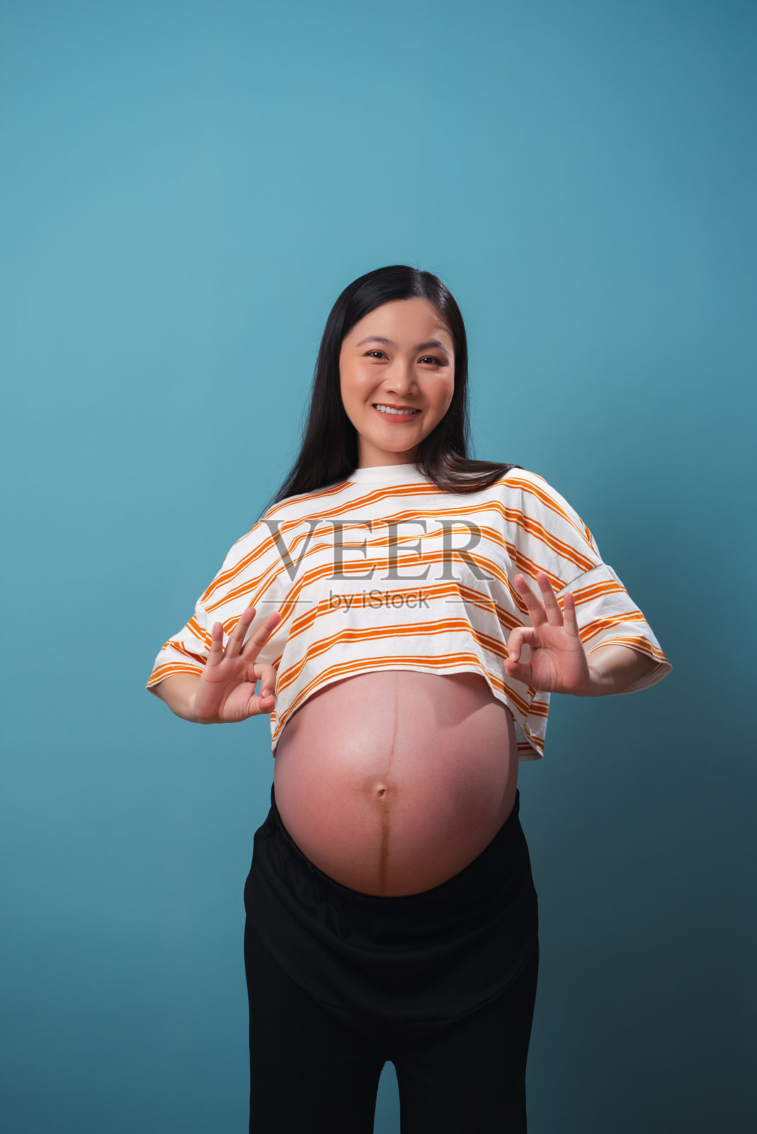 亚洲孕妇在蓝色背景下做出OK手势。照片摄影图片