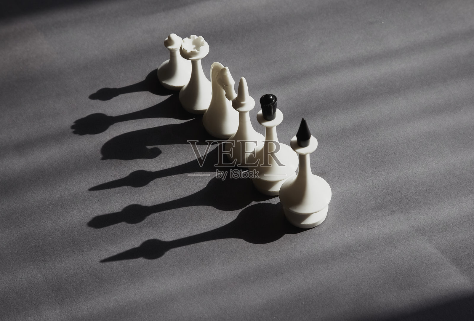 阳光下排成一行的白色棋子，在灰色背景上投射出黑色阴影，准备行动，所有可能性，善良的阴影面。照片摄影图片