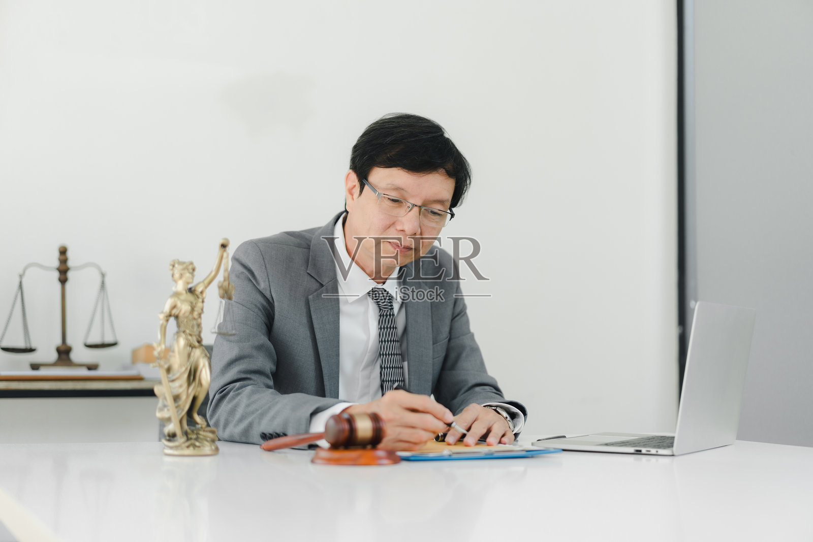 一位穿着西装的专业人士正在桌子上使用笔记本电脑，旁边有法律符号。照片摄影图片
