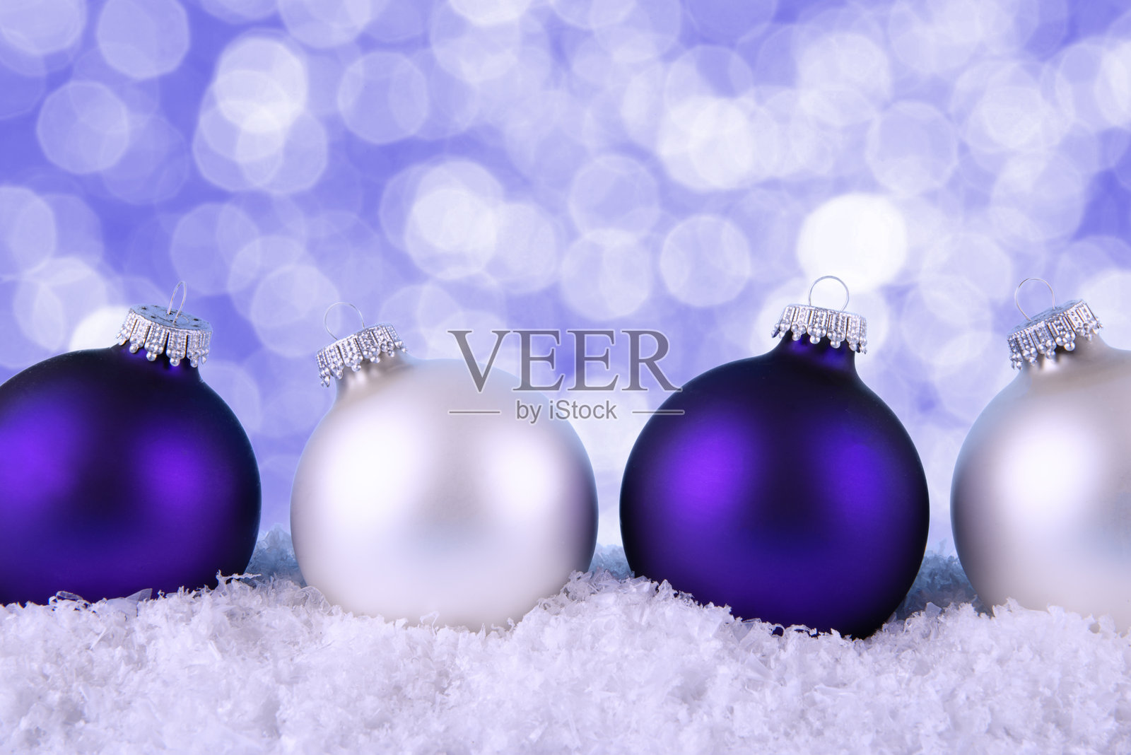 四个圣诞装饰品排成一行，颜色交替，放置在人造雪的床上。背景呈现出散景效果，营造出节日和梦幻的氛围。照片摄影图片