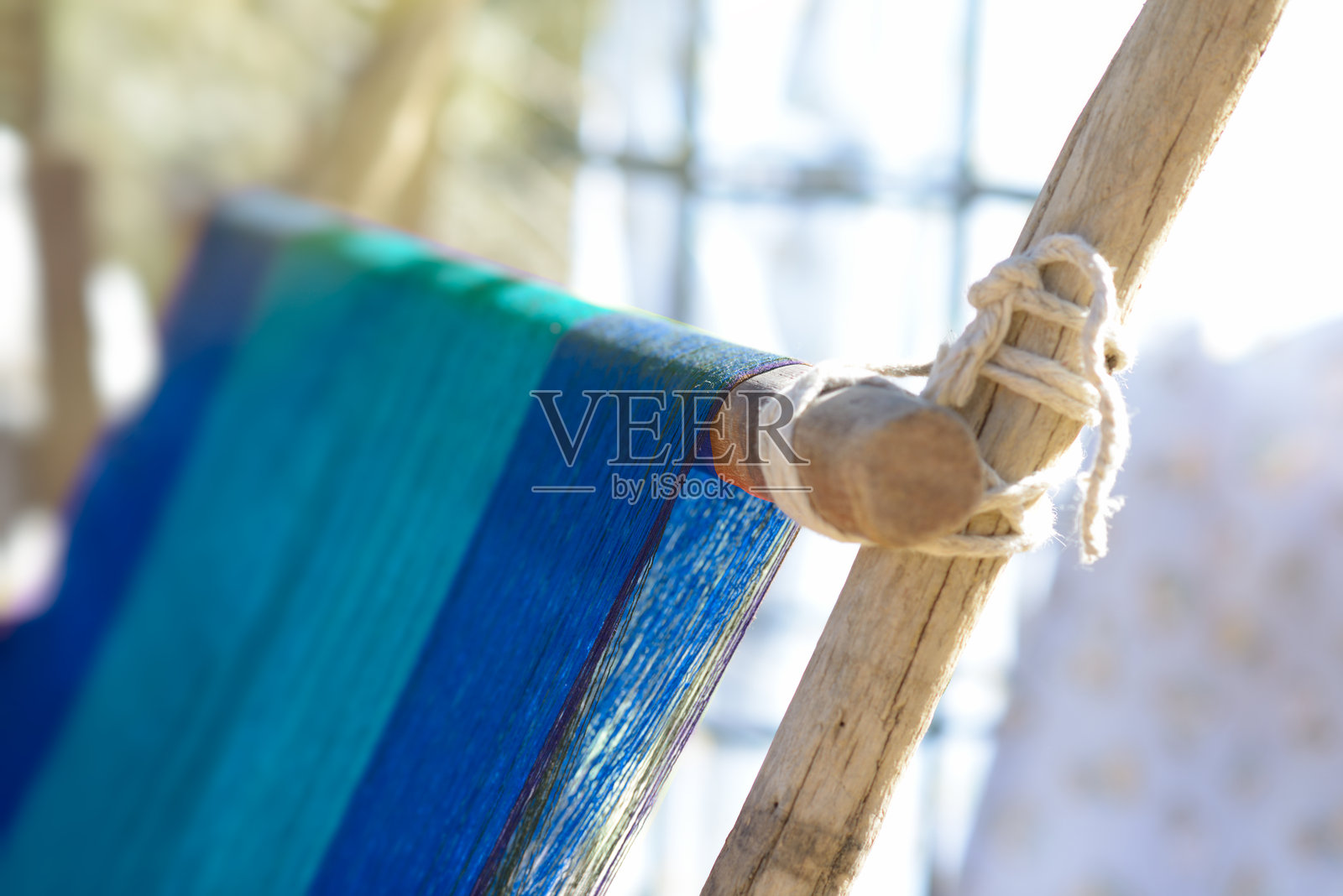 在阳光明媚的环境中，蓝色和绿色的布料在木织机上编织。照片摄影图片