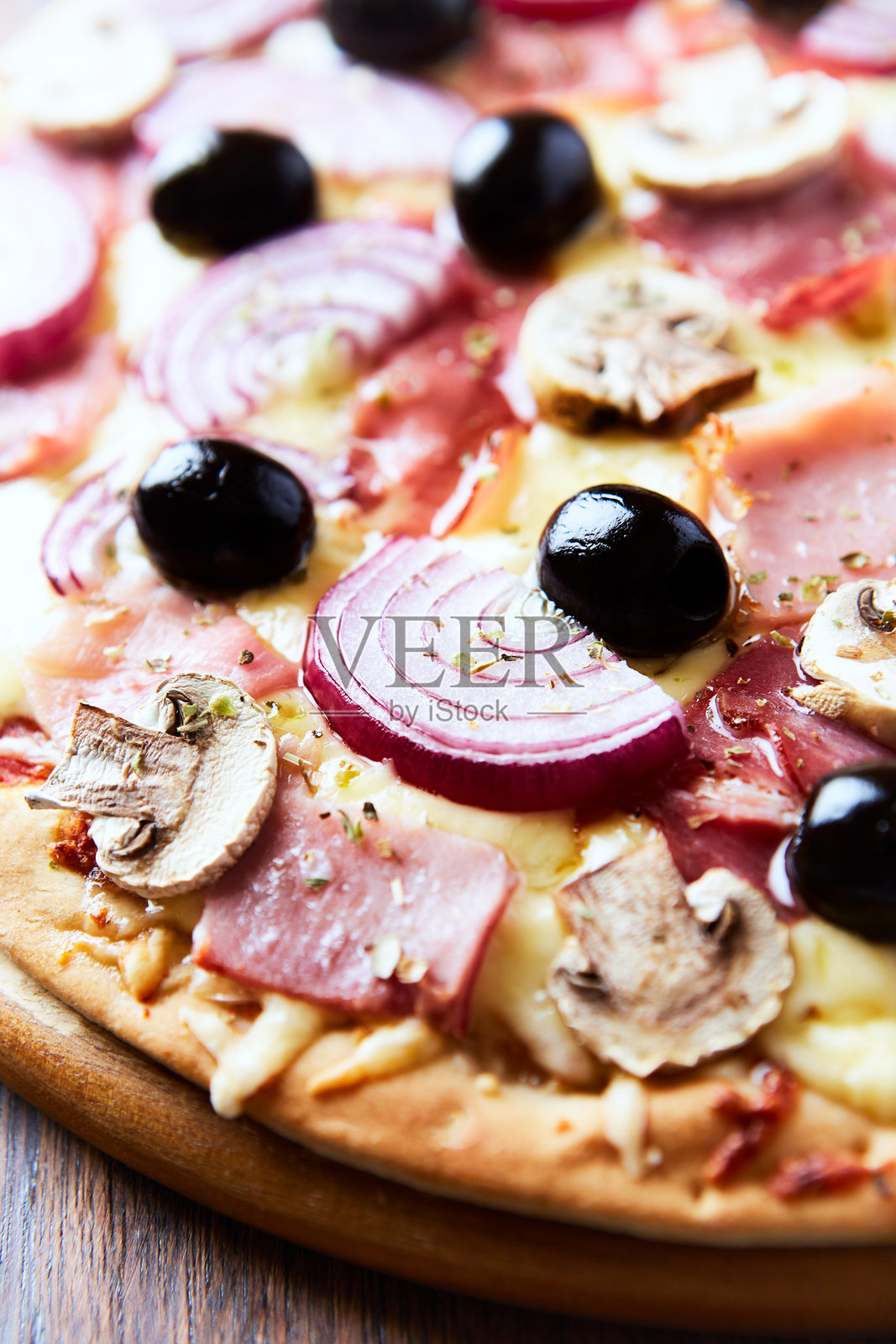 木质背景上的比萨饼，配有火腿、香菇、马苏里拉奶酪、黑橄榄和新鲜的芝麻菜。特写。照片摄影图片