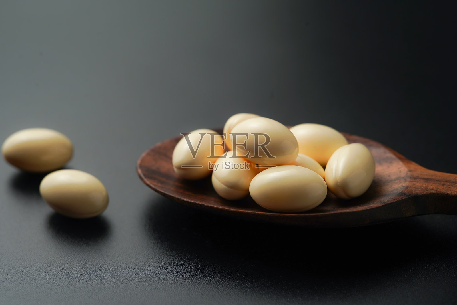 木勺中的白色软胶囊，含有维生素E、鳕鱼肝油、DHA和鱼油Omega-3照片摄影图片