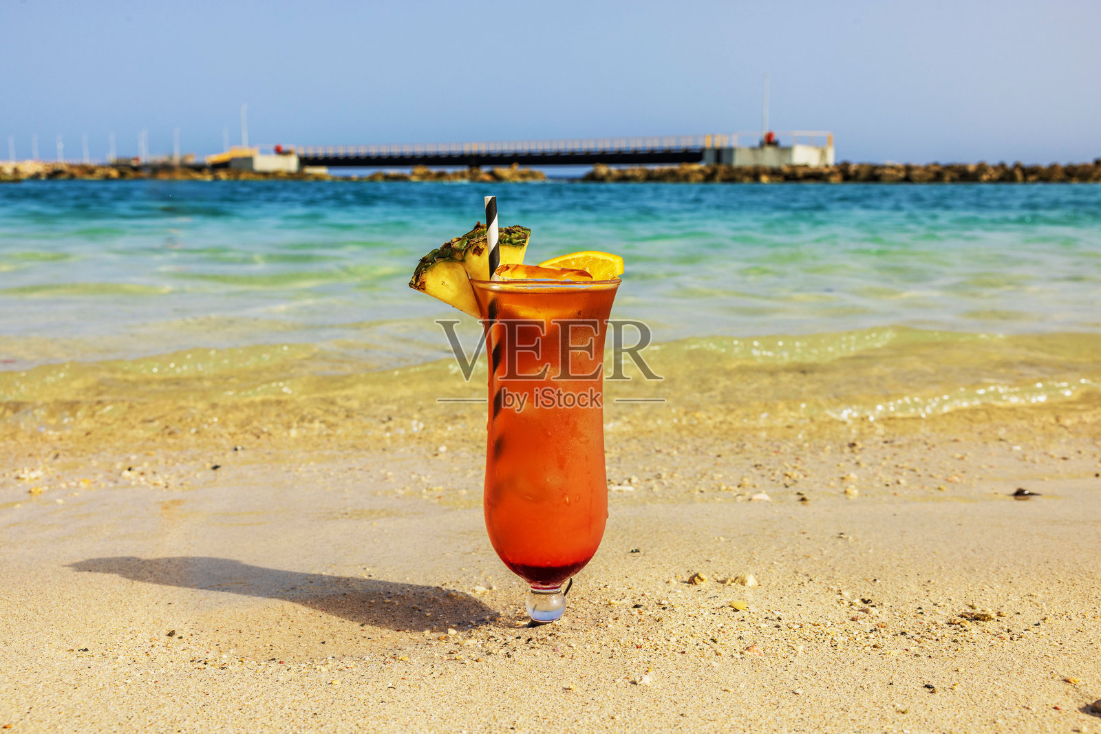 清爽的热带鸡尾酒，配有菠萝和橙子装饰，放置在沙滩上，背景是碧蓝的加勒比海，库拉索。照片摄影图片