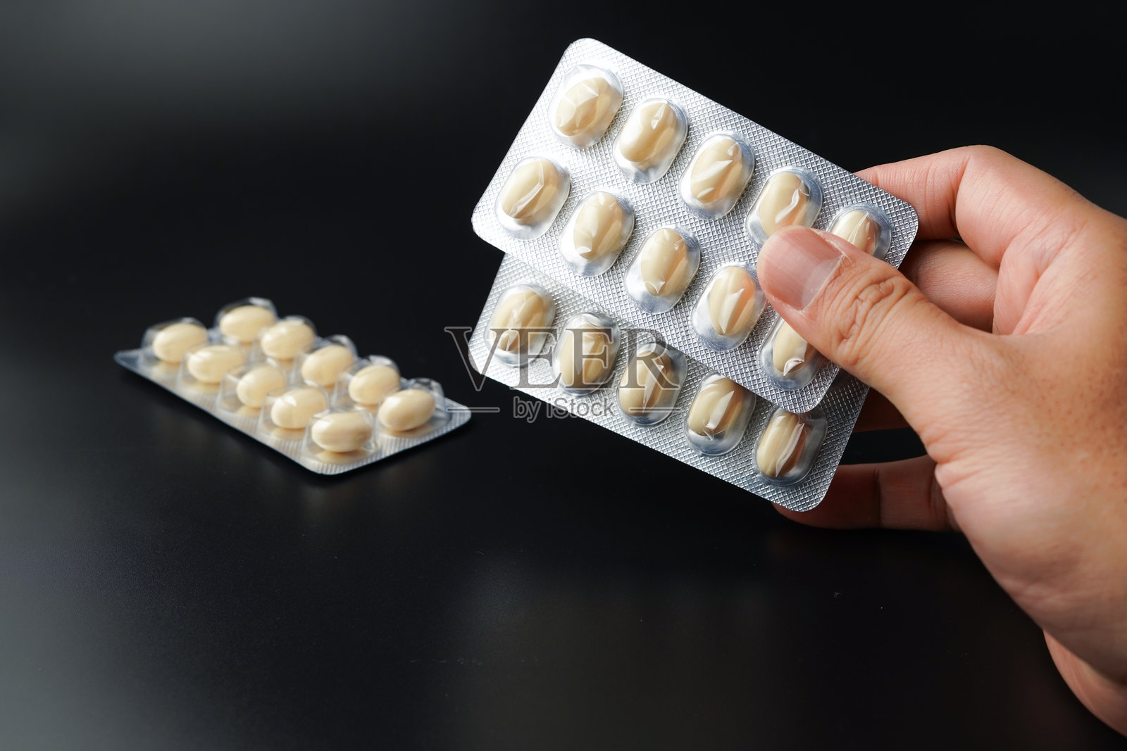 男子手持含有Omega、维生素E、鳕鱼肝油和DHA的白色软胶囊鱼油泡罩包装。照片摄影图片