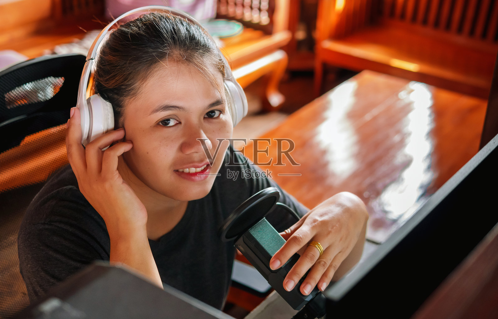 微笑且积极的亚洲女性播客主持人戴着耳机，在录音室进行她的广播播客，并对着镜头微笑。照片摄影图片