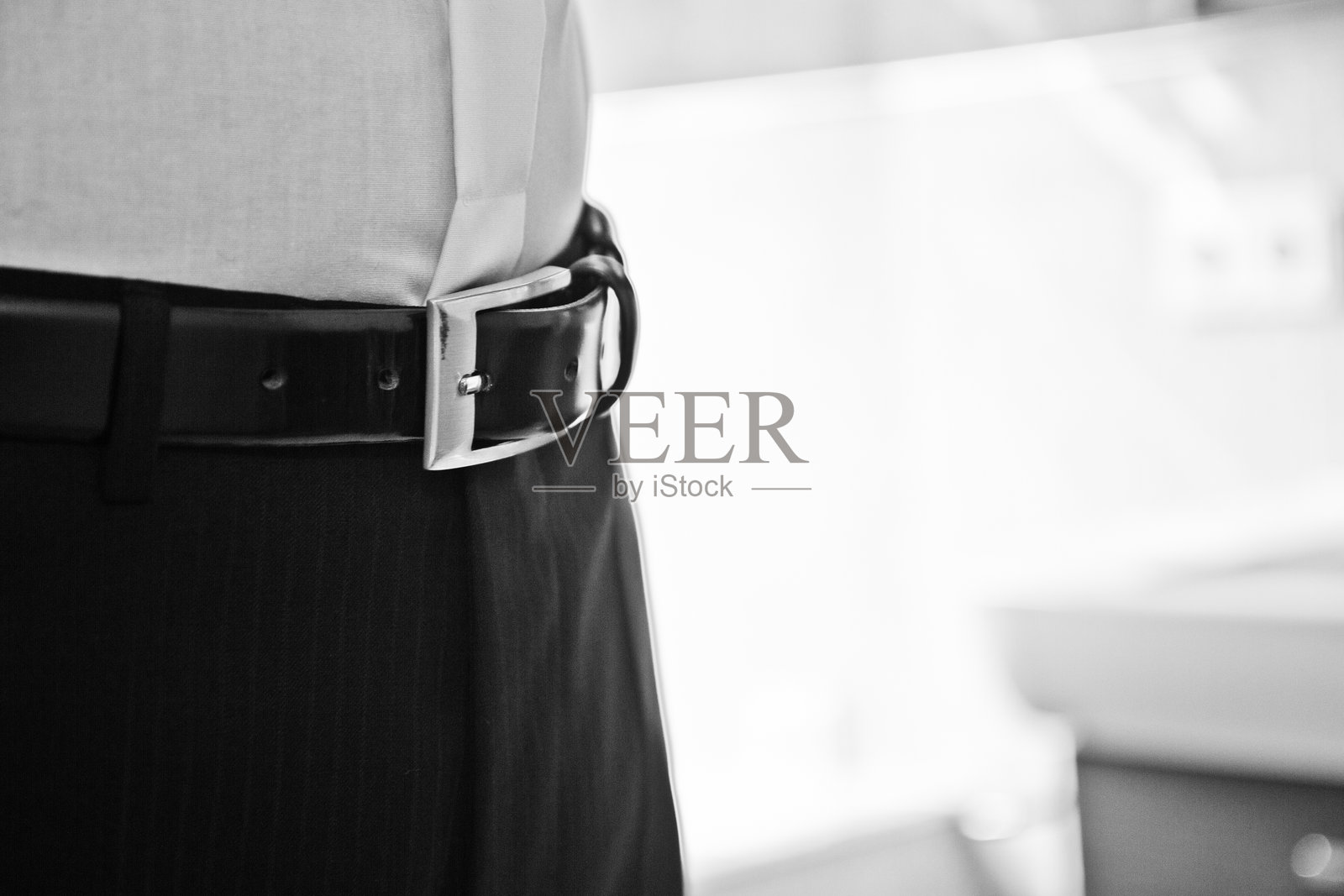 在光线明亮的室内空间中，男子佩戴着银色扣环的黑色腰带，正值白天。照片摄影图片