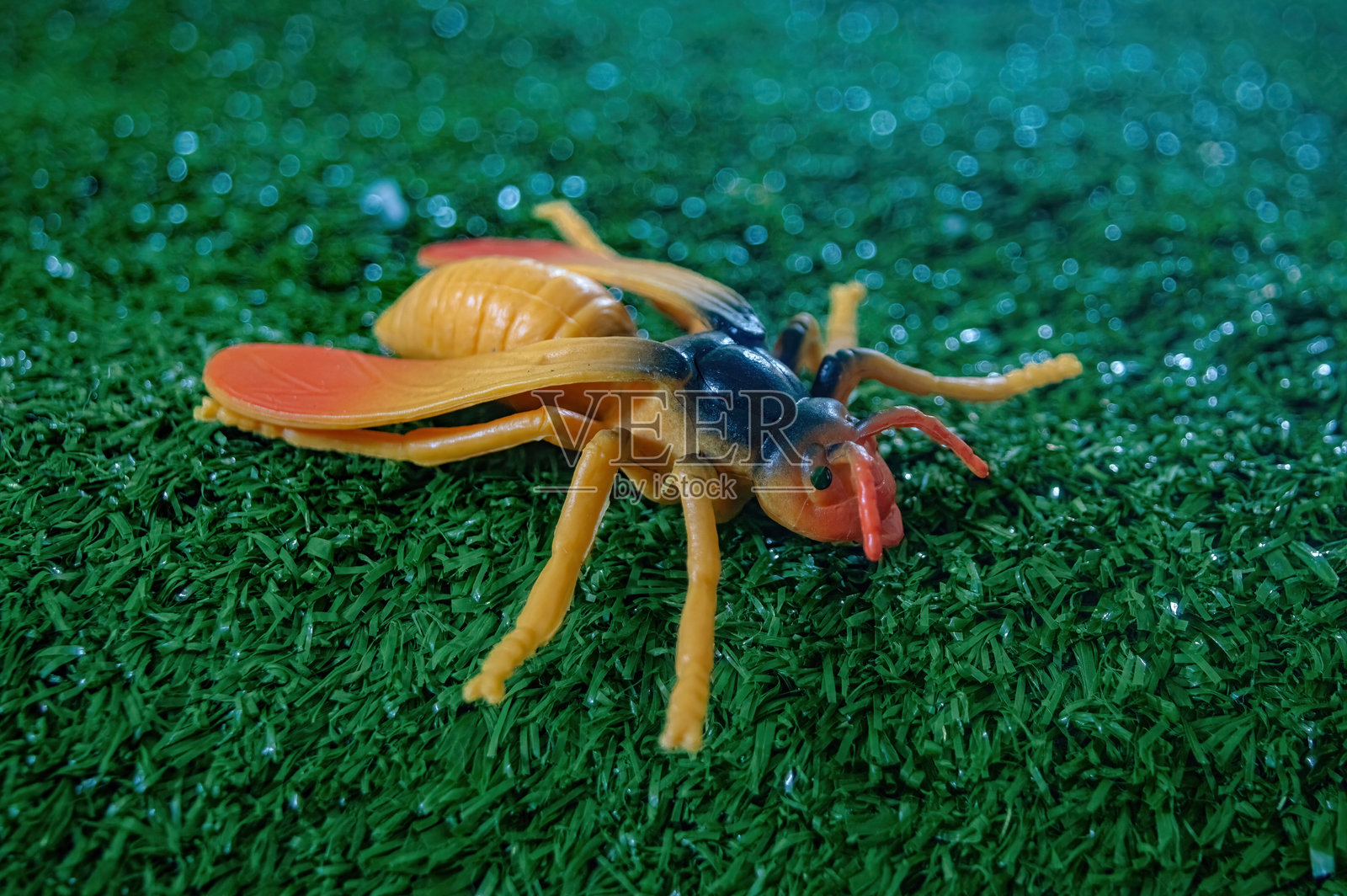 一个色彩鲜艳的逼真玩具昆虫躺在人造草坪上，适合教育用途或儿童玩耍。照片摄影图片