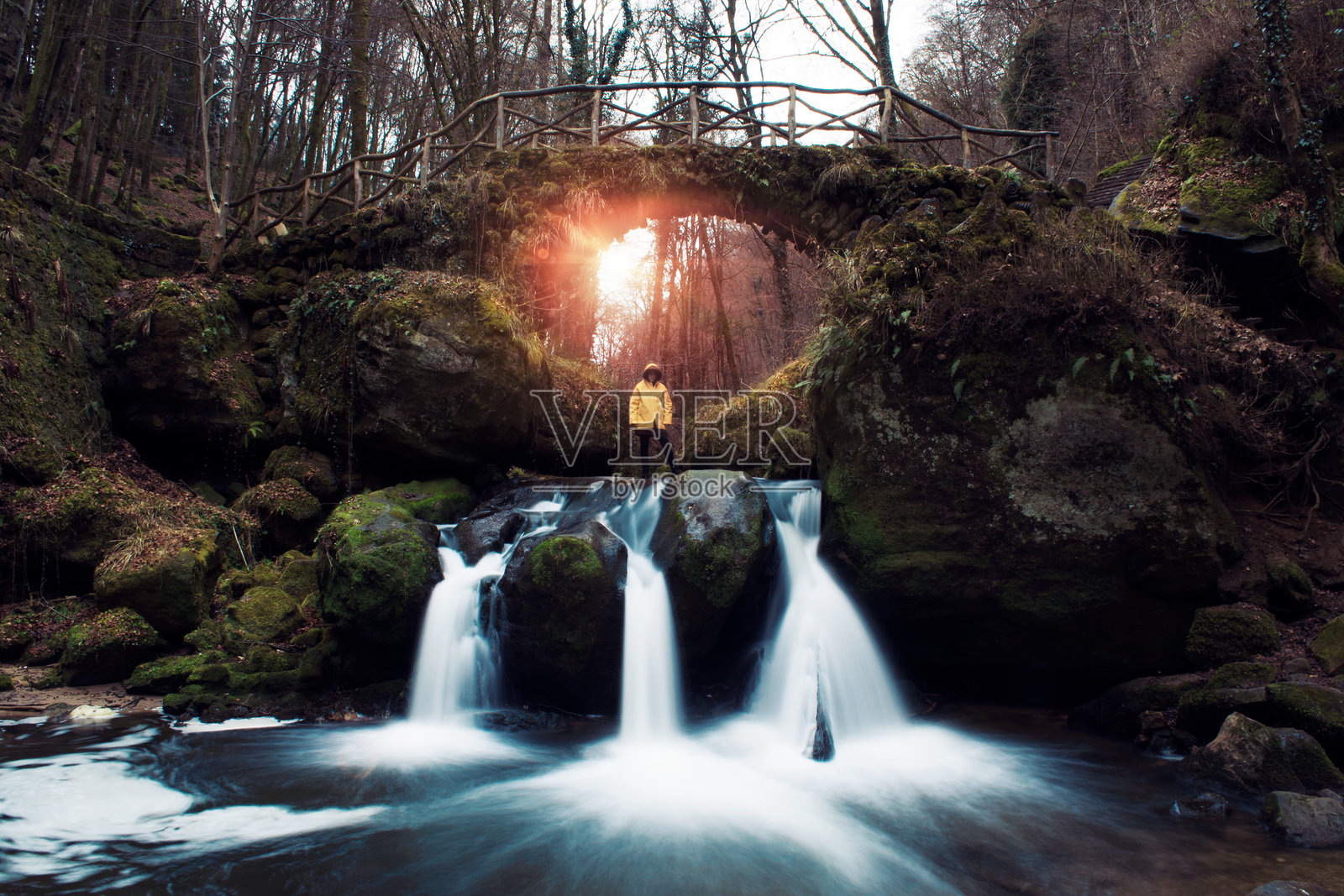 低角度视图的女性站在森林中的岩石上，背景是瀑布。照片摄影图片