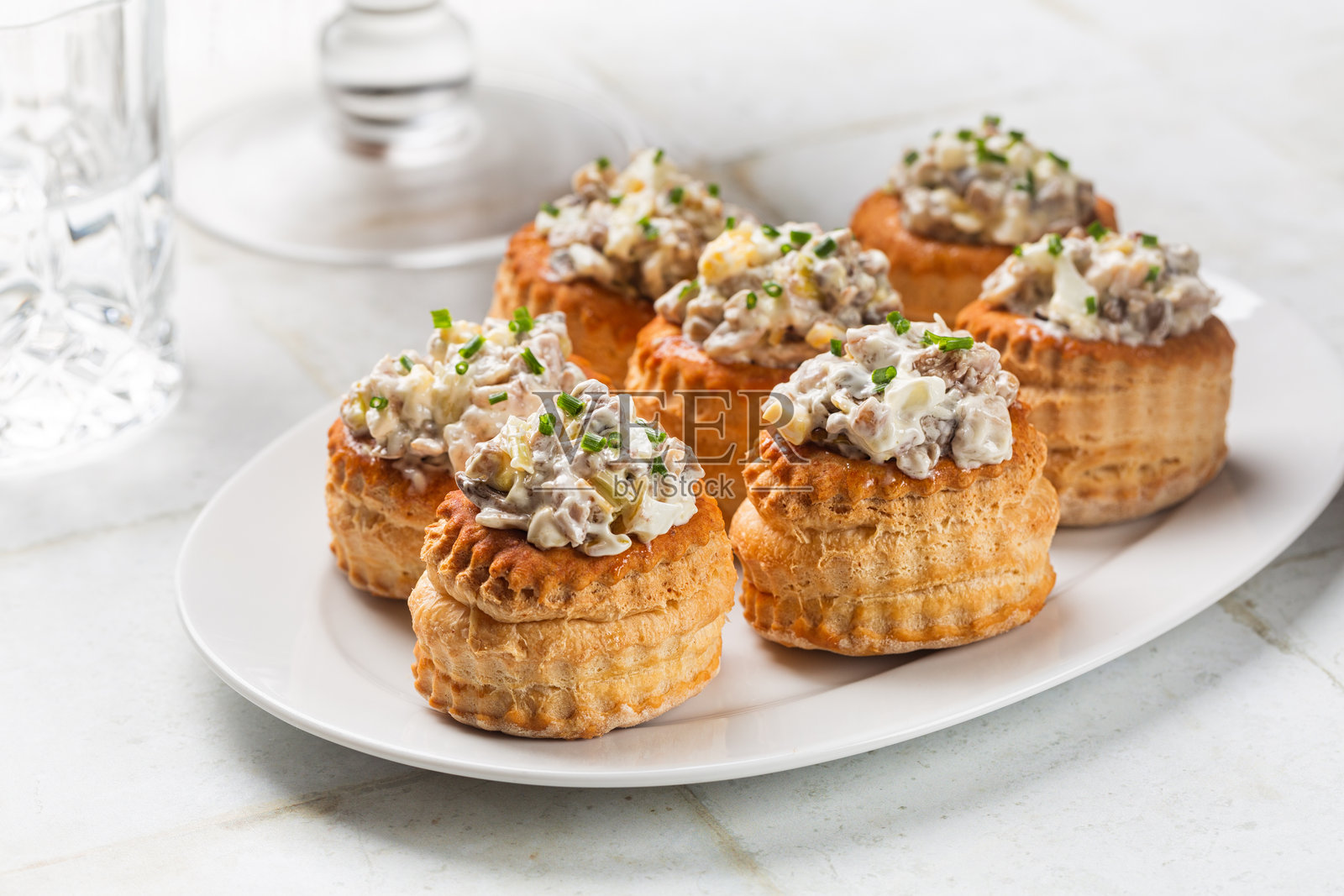 白色桌子上摆放着奶油鸡肉蘑菇泡芙。填充的酥皮壳，旁边有饮料杯。节日季节的开胃菜，迷你小吃。照片摄影图片