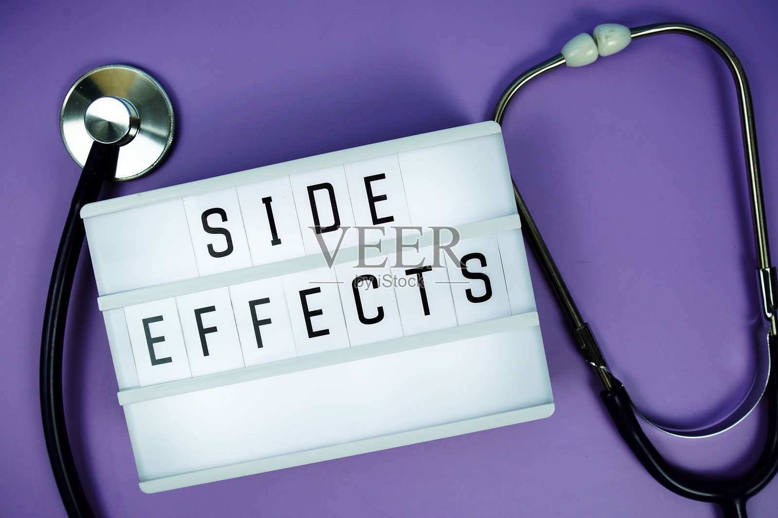 紫色背景上的LED灯箱字母板文字“副作用”和听诊器，医疗概念照片摄影图片