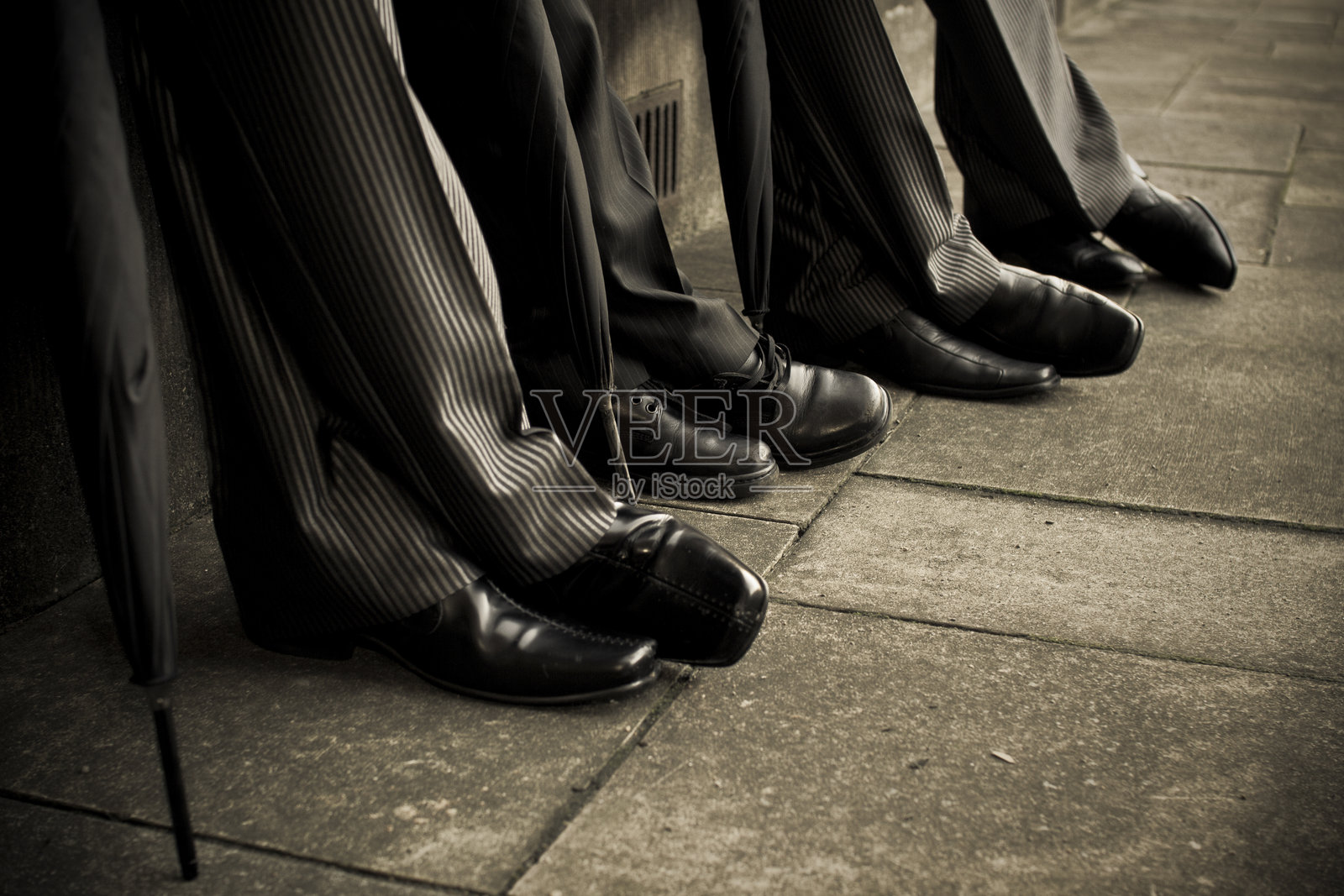 三位身着正式服装的男士在城市人行道上休息，脚下是优雅的鞋子。照片摄影图片