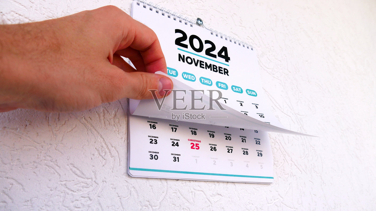 一只男人的手翻动墙上日历的十一月页面，接着翻到标有2024年圣诞节的下一页。照片摄影图片