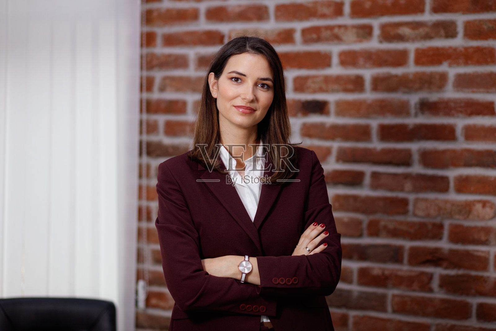 自信的女商人穿着酒红色西装，站在砖墙前照片摄影图片