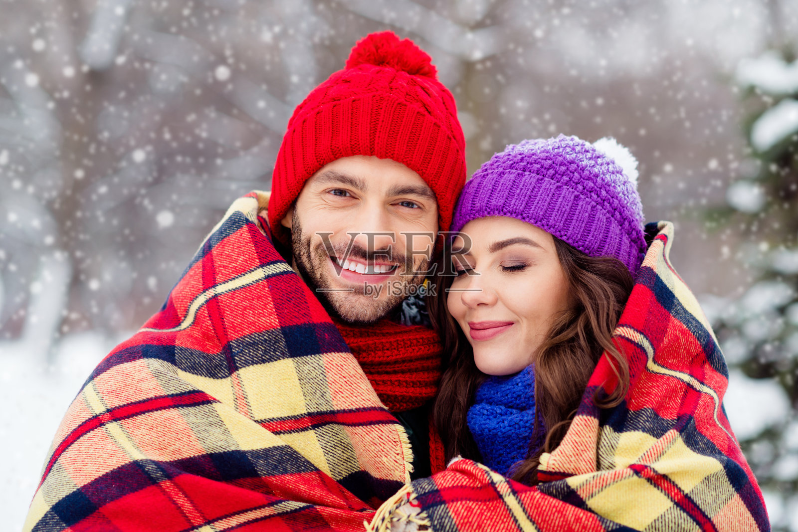 梦幻般的可爱情侣穿着背心，微笑着拥抱，在户外森林的雪地上漫步，身下是格子图案的被子。照片摄影图片
