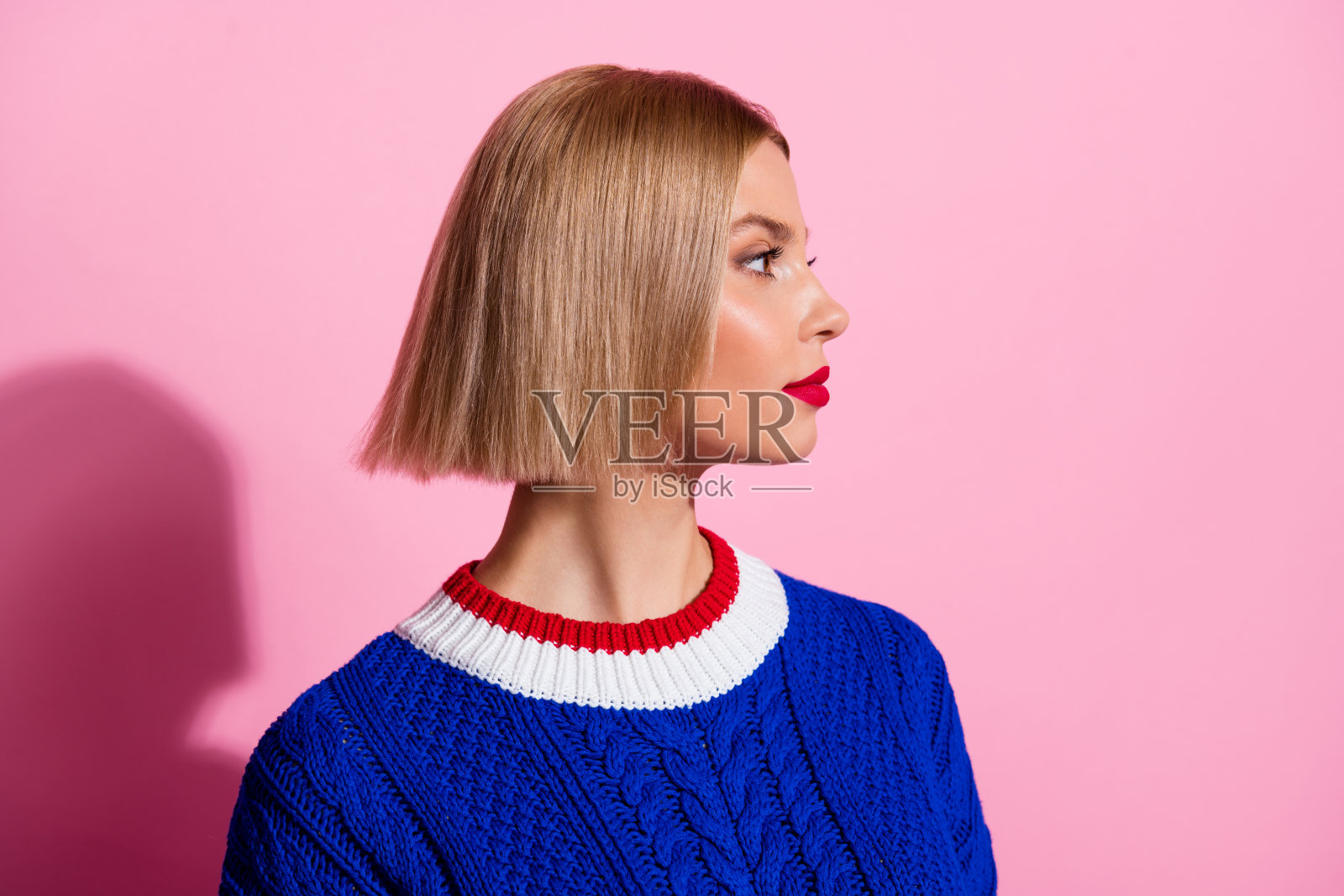 年轻女士的侧面肖像，穿着时尚的蓝色服装，背景为粉色，显得空旷。照片摄影图片