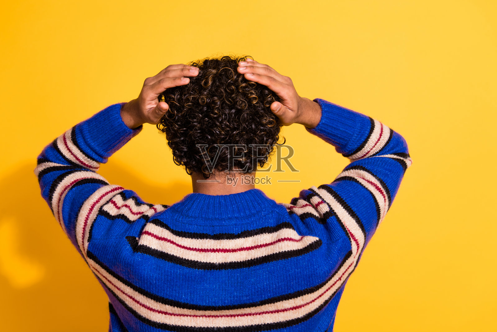 年轻帅气男性背影肖像，手触头发，穿着时尚的蓝色条纹服装，背景为黄色。照片摄影图片