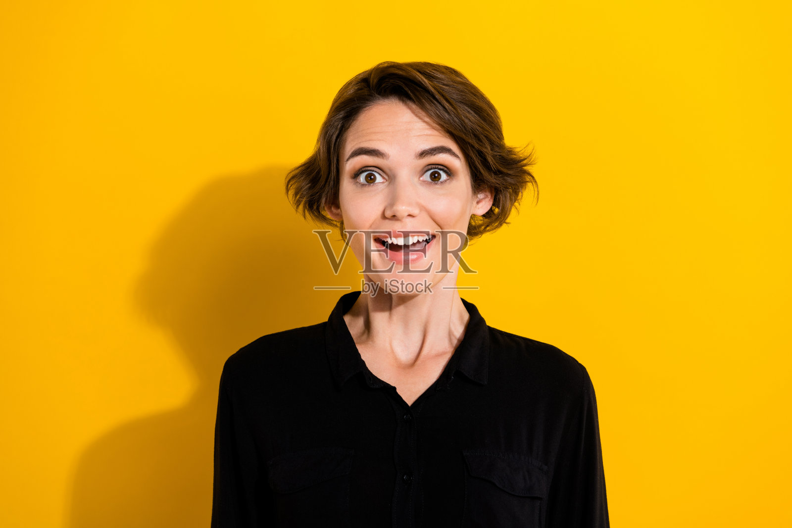 一位欢呼的千禧一代短发女士穿着黑色衬衫，背景为黄色。照片摄影图片