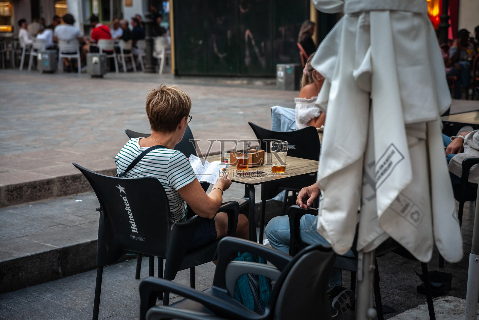 一位女性游客在咖啡馆的露台上阅读关于瓦伦西亚的旅游指南，同时喝着啤酒。瓦伦西亚是一个日益增长的旅游目的地。照片摄影图片