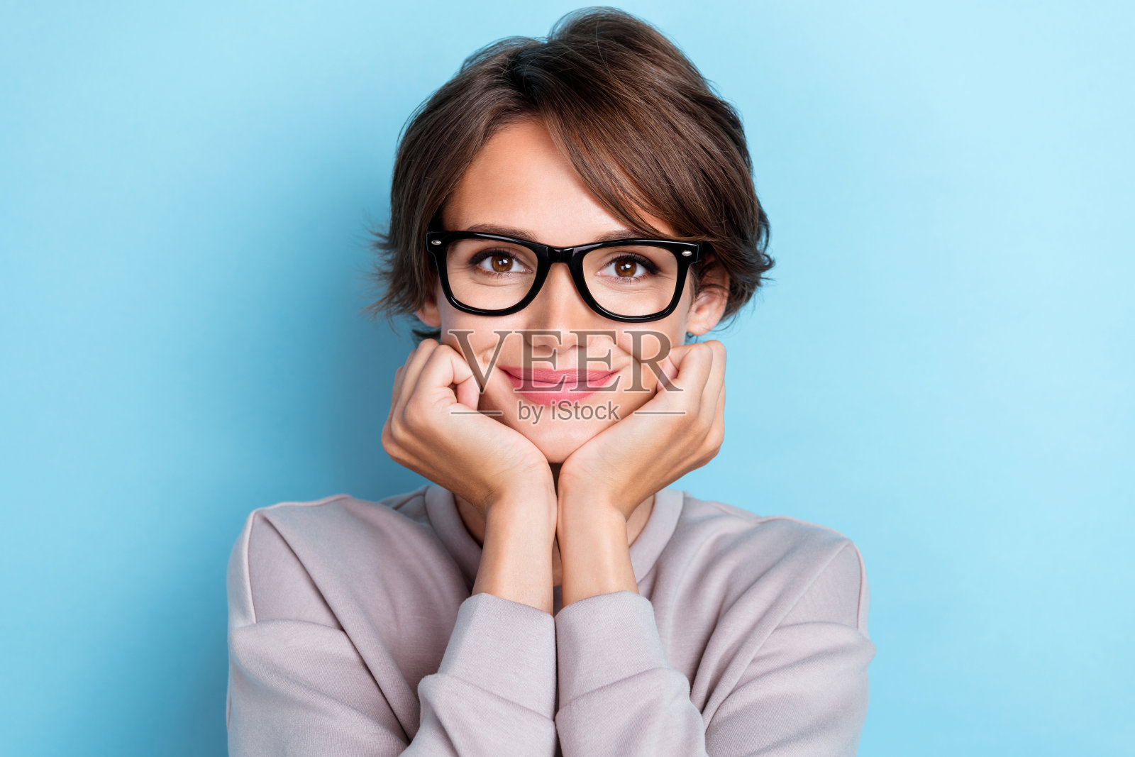 甜美可爱温柔的女士用手臂托着下巴，轻触颧骨，佩戴时尚眼镜，穿着时尚服装，背景为蓝色。照片摄影图片