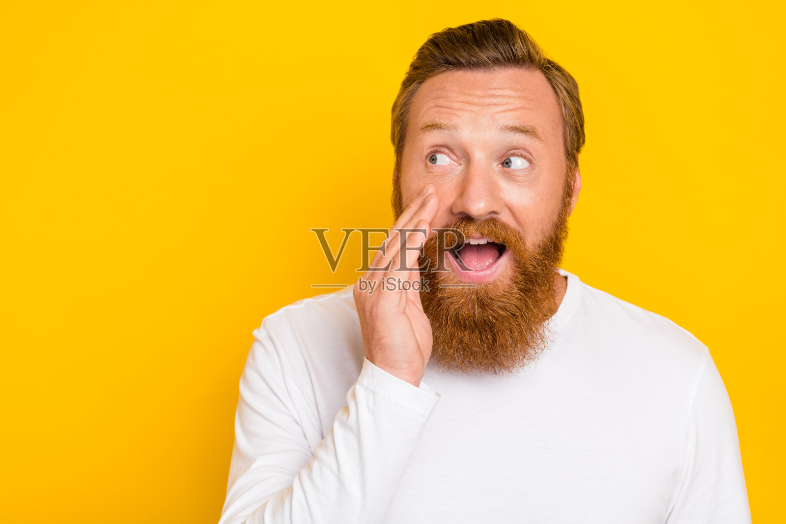 年轻男子的照片肖像，捂住嘴巴讲秘密，目光投向空旷的地方，穿着时尚的白色毛衣，背景为黄色。照片摄影图片