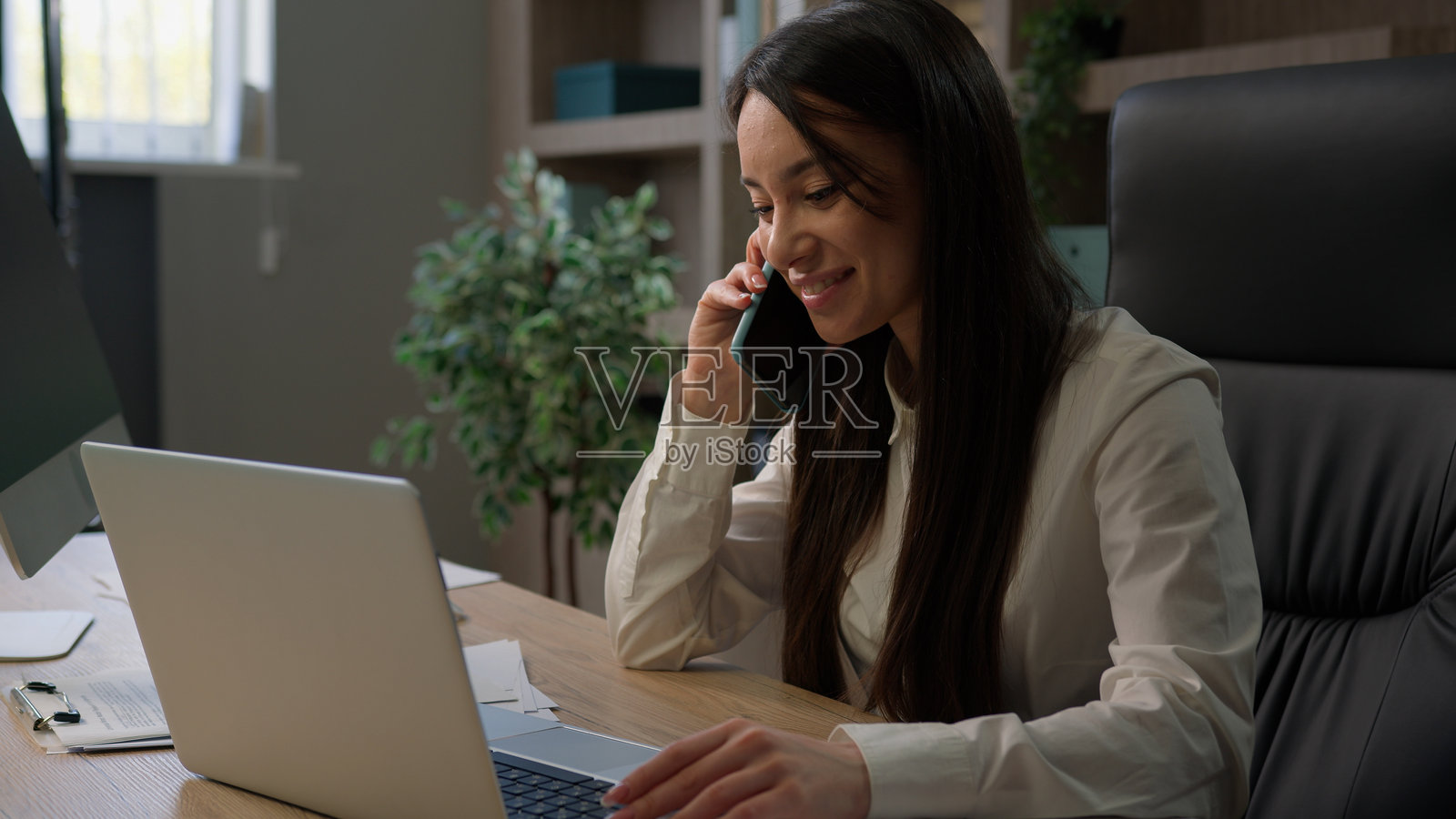 白人女商人在办公室忙碌地多任务处理，使用笔记本电脑在线工作，接听手机电话，撰写文件，与客户交谈。照片摄影图片