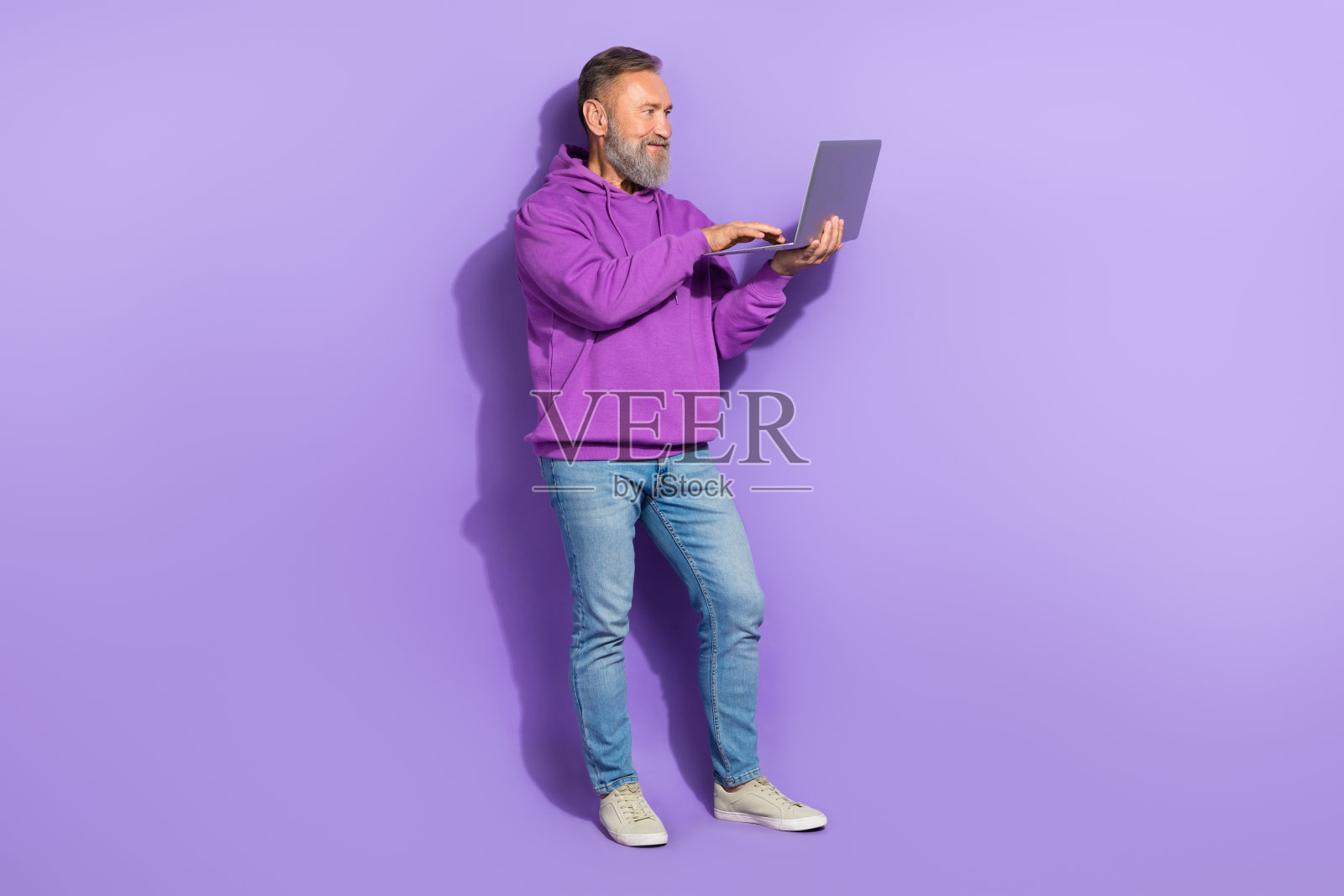 全身照，退休的现代男性穿着紫色连帽衫和牛仔裤，在紫色背景下进行远距离对话。照片摄影图片