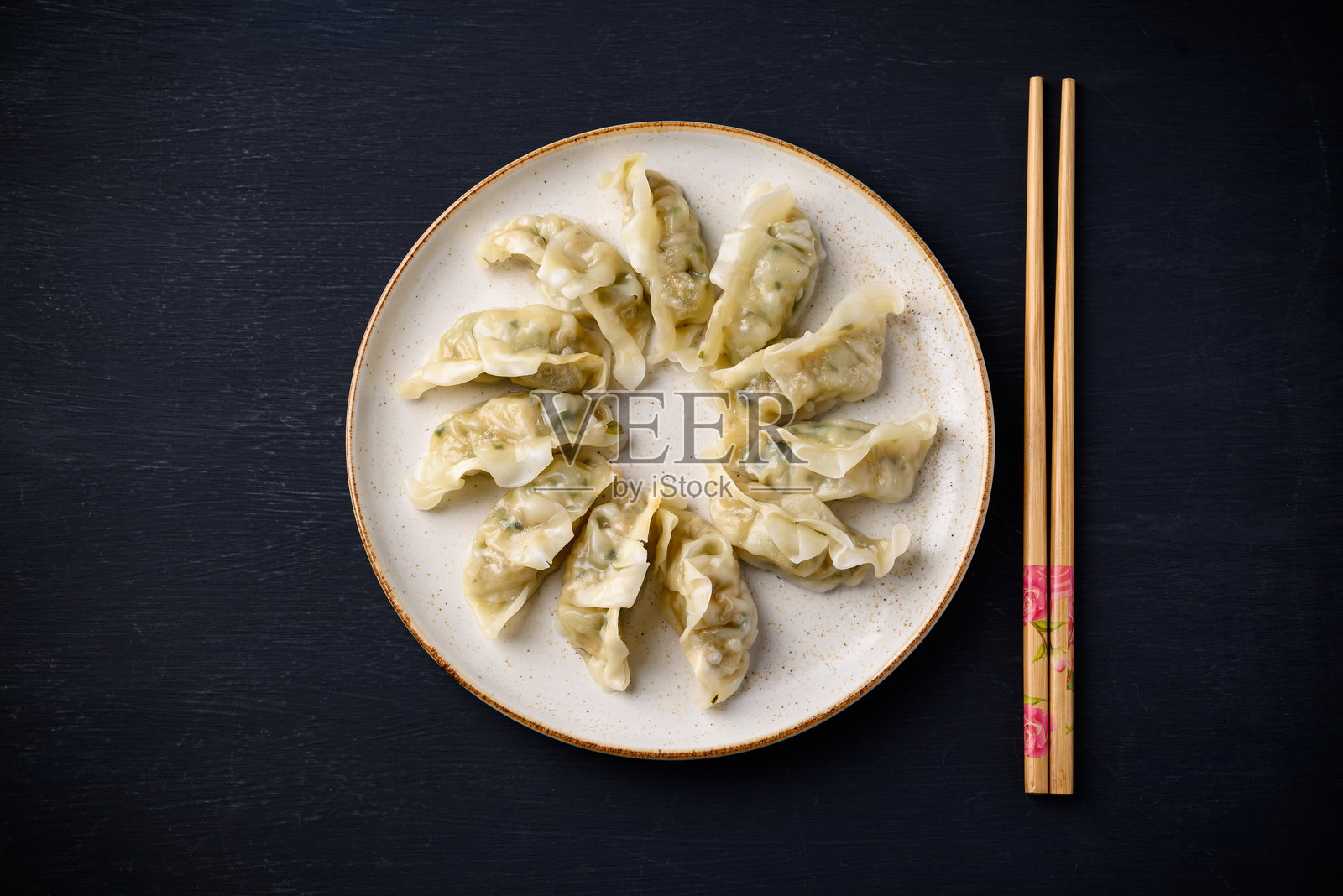 黑色背景上的盘子里放着蒸饺，内馅为猪肉和蔬菜，旁边有筷子。照片摄影图片