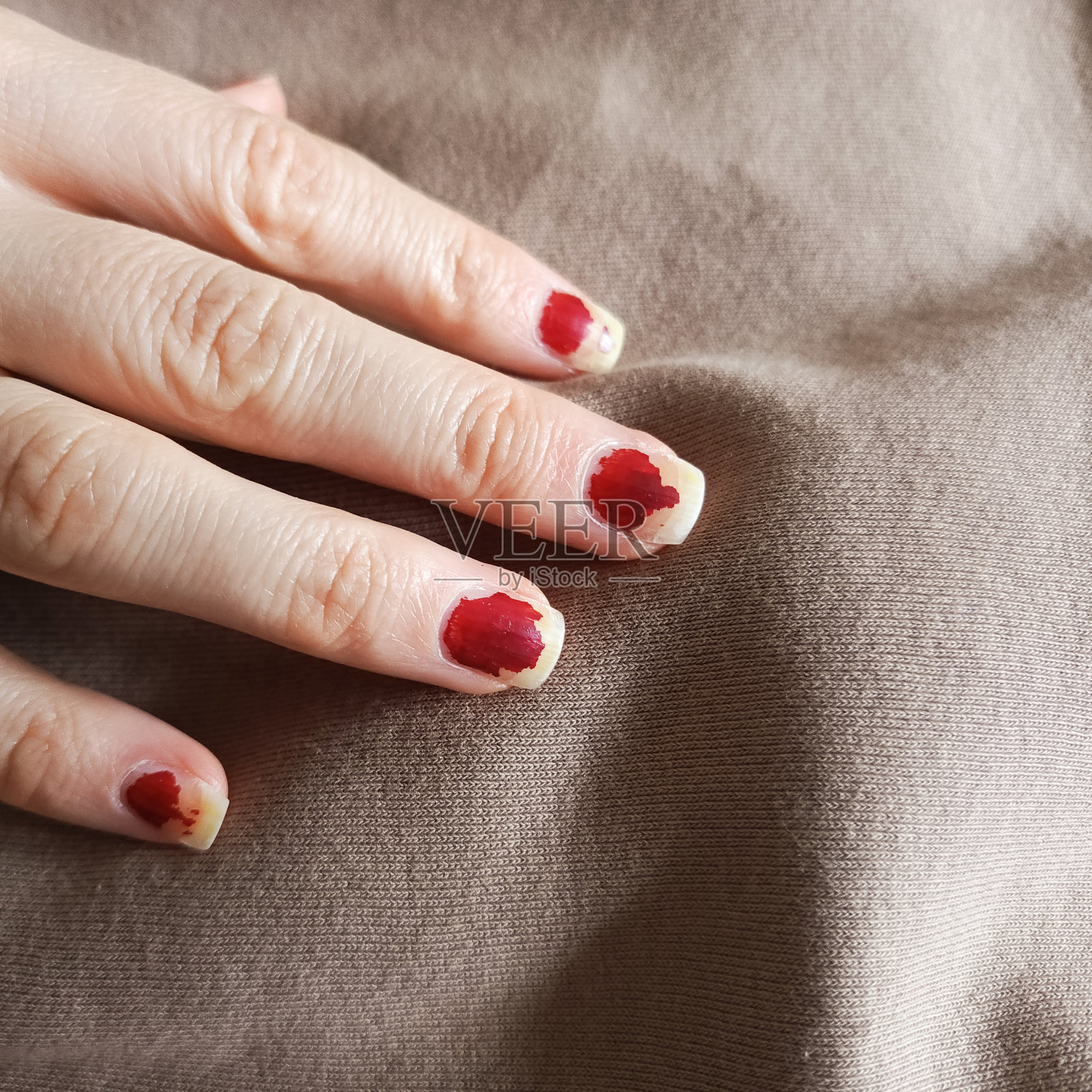 一只女性手上的毁坏美甲。剥落的红色指甲油。沙龙服务质量差的概念。照片摄影图片