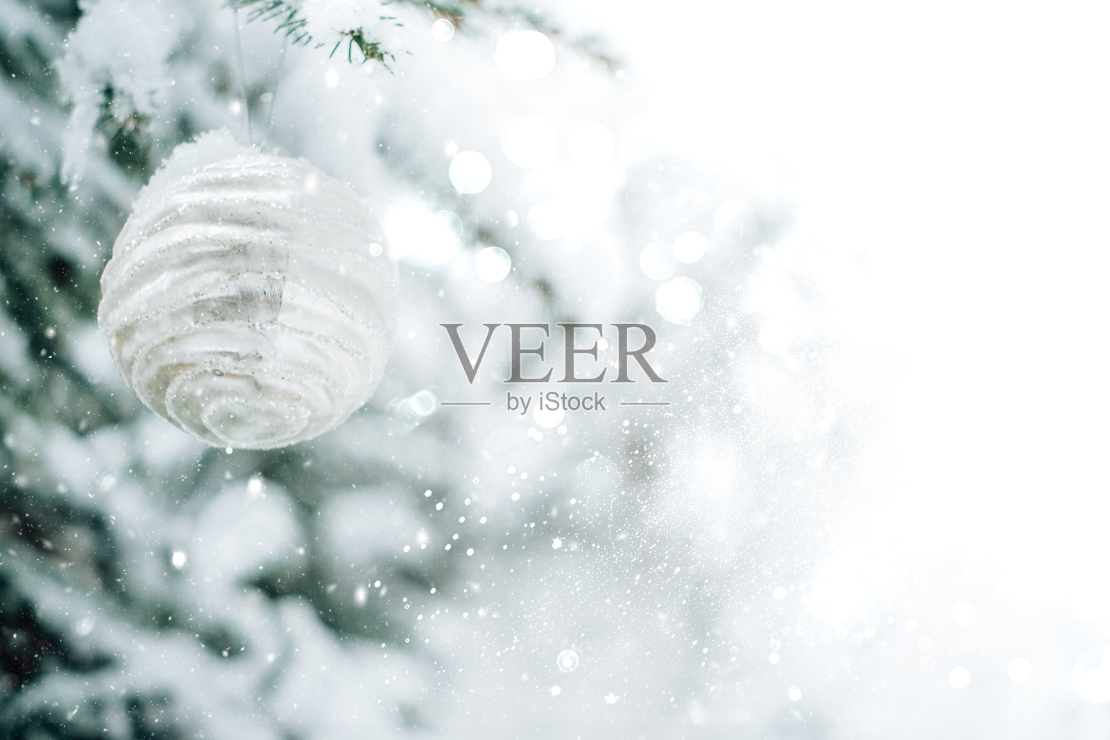 白色调的圣诞背景，带有散景、眩光和雪花。银色圣诞球挂在雪-covered的松枝上，背景是雪白的森林。银色和白色调的冬季假日壁纸。照片摄影图片